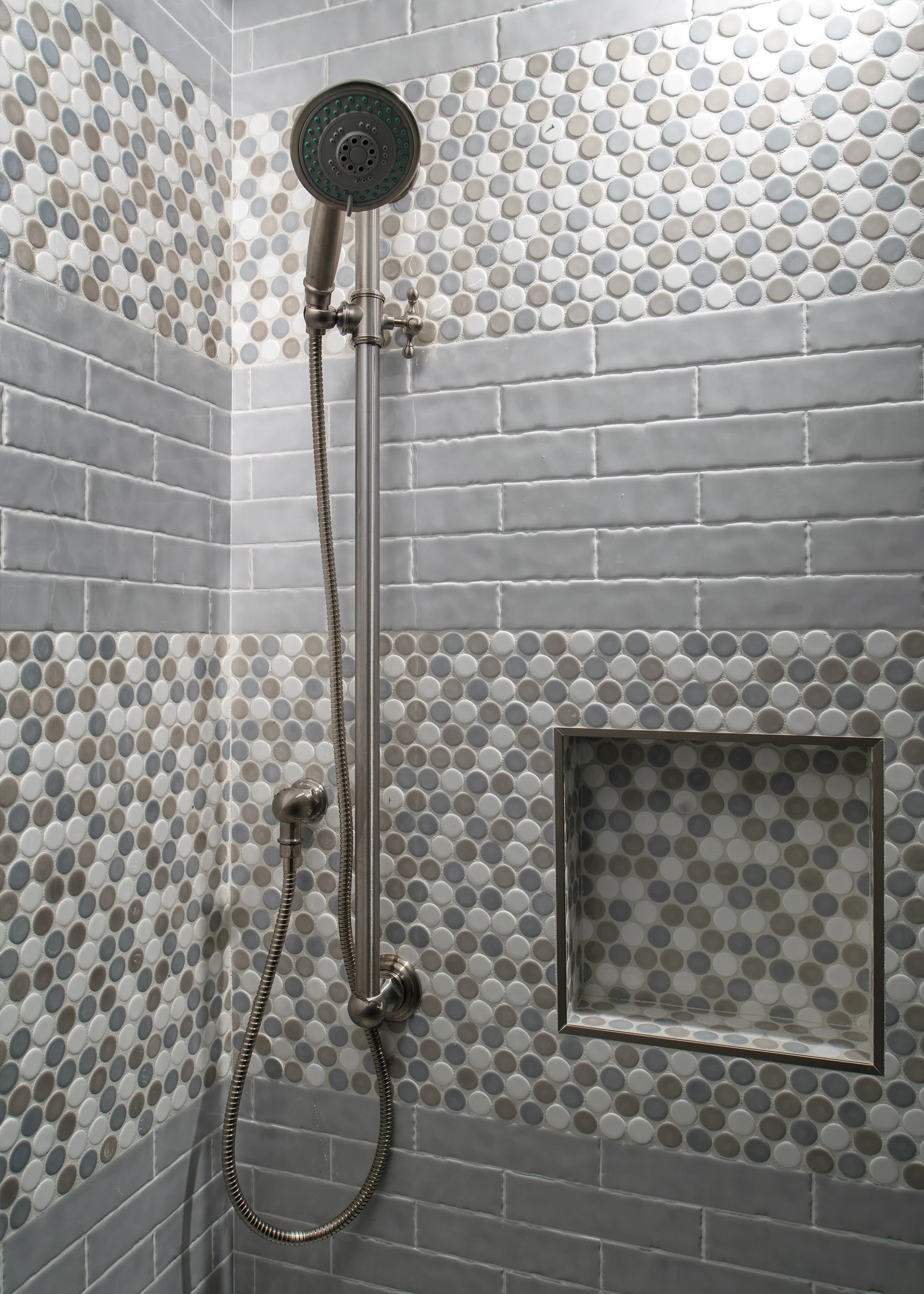 Showerhead and hose mounted on tiled wall in a shower area with a built-in niche.