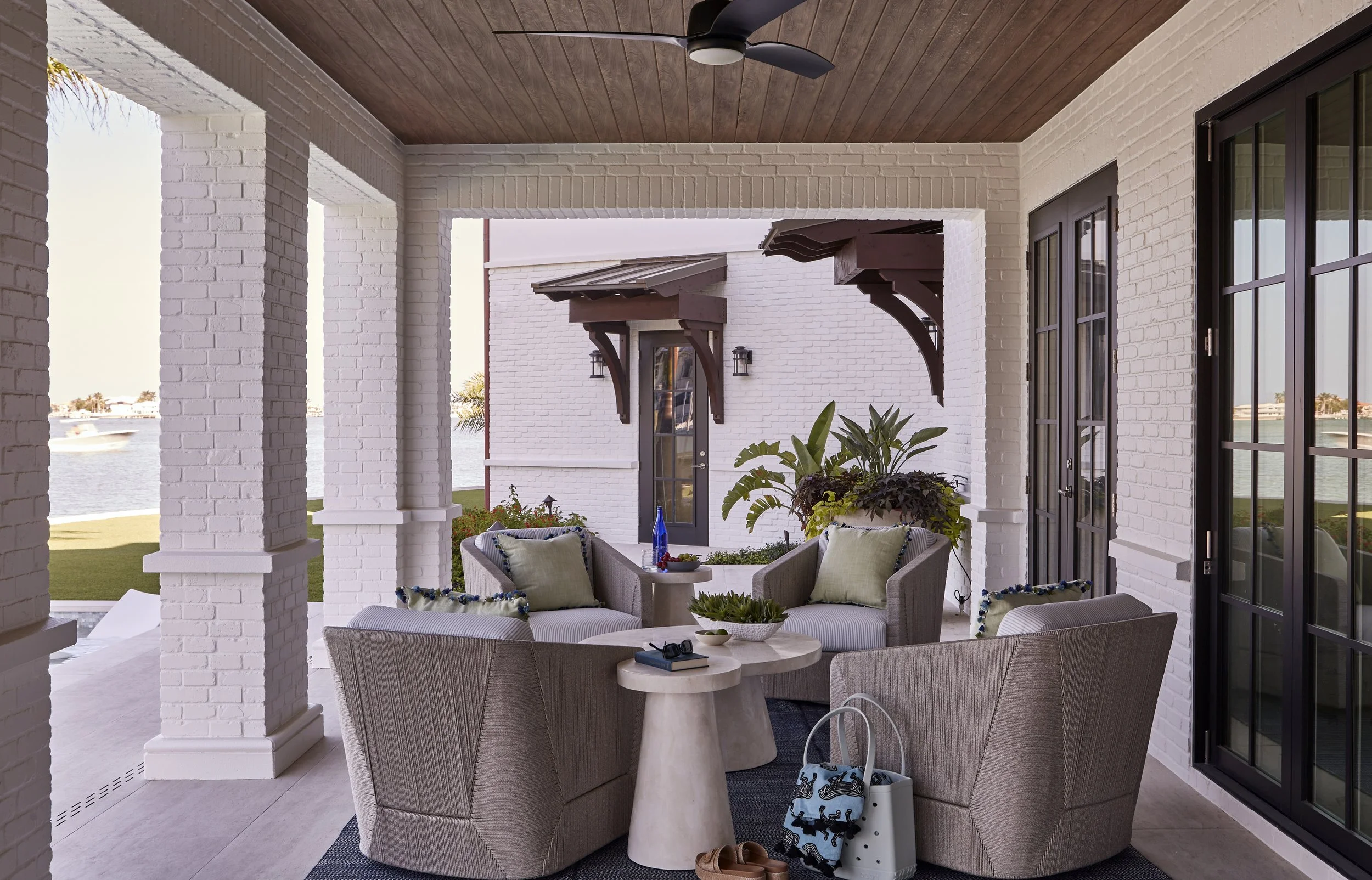 Outdoor patio with round seating area, cushions, plants, and view of water and boats in the background
