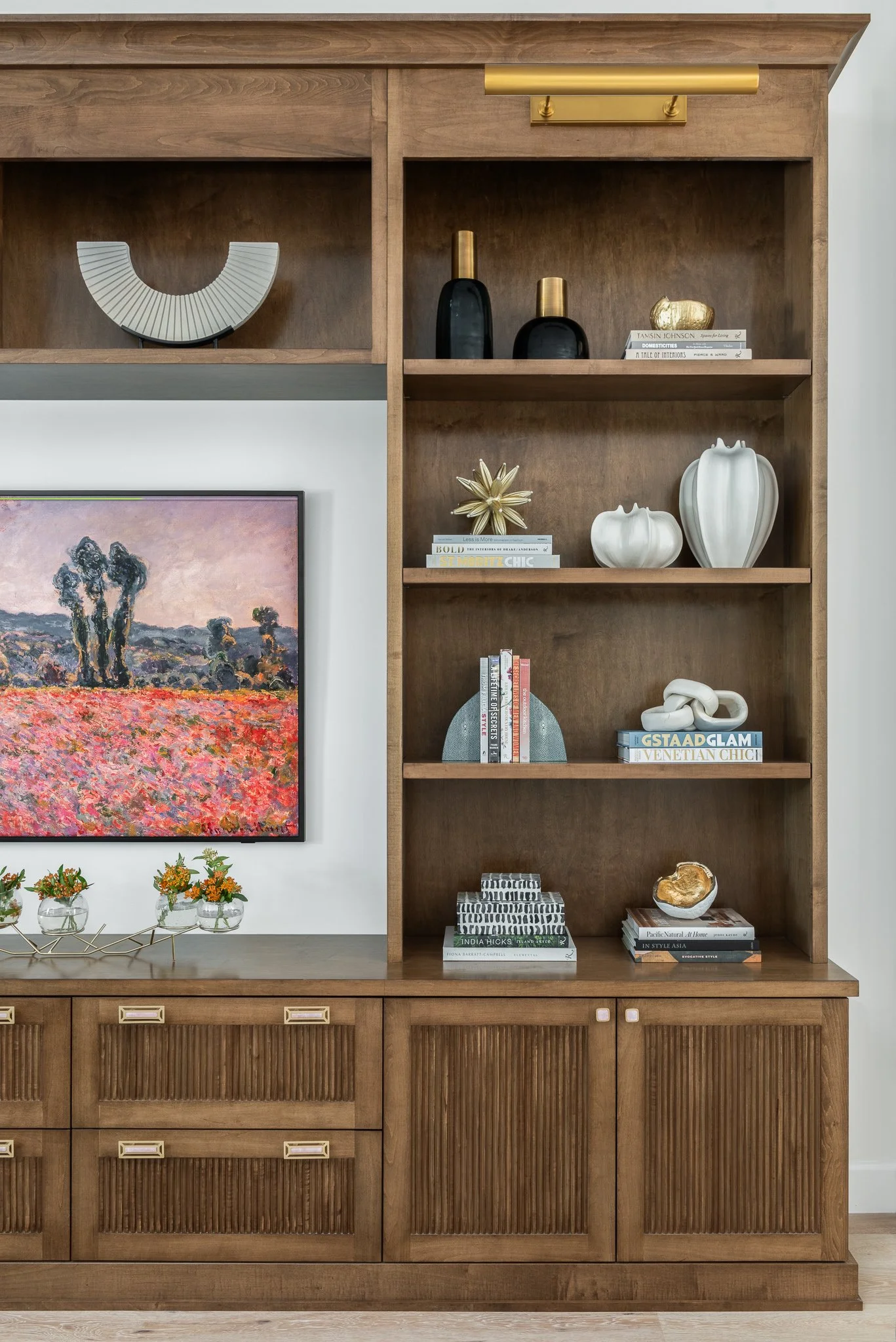 A wooden cabinet with open shelves displays decorative vases, books, and sculptures, with a colorful landscape painting hanging to the left.