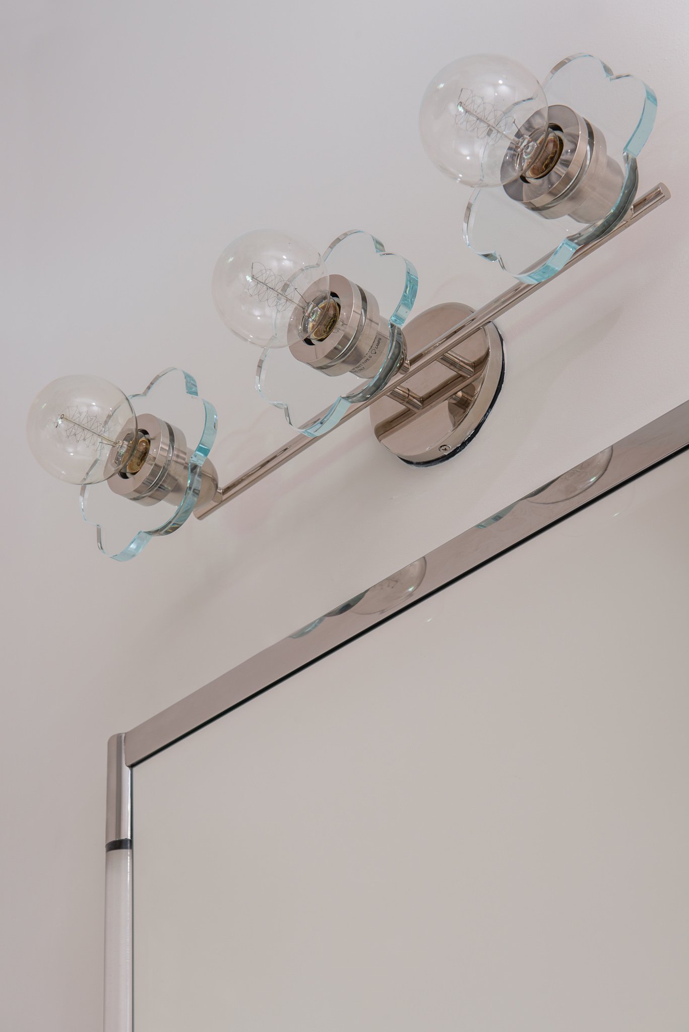 Close-up of a modern ceiling light fixture with three exposed filament bulbs in glass holders, mounted on a metallic rod on a white ceiling.
