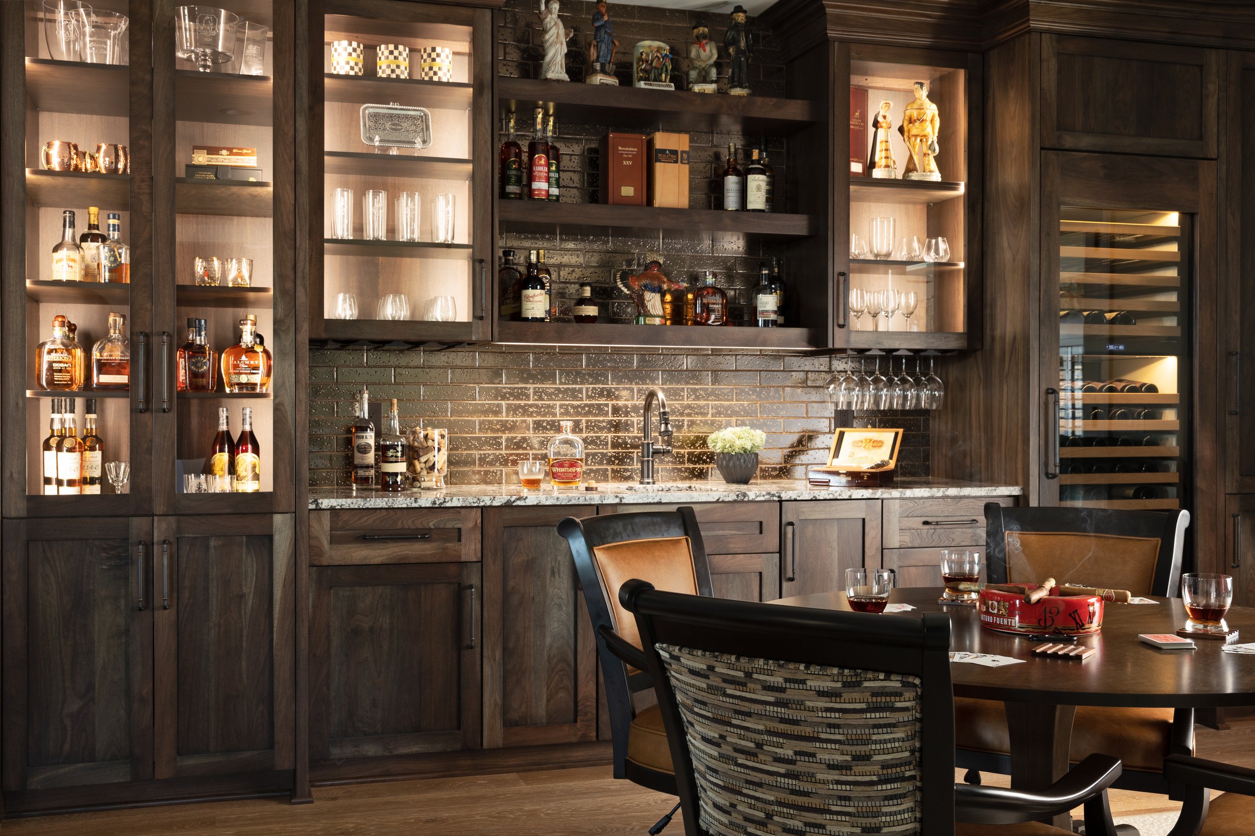 Home bar area with dark wood cabinets, glassware, liquor bottles, and a round table with drinks and board game pieces.