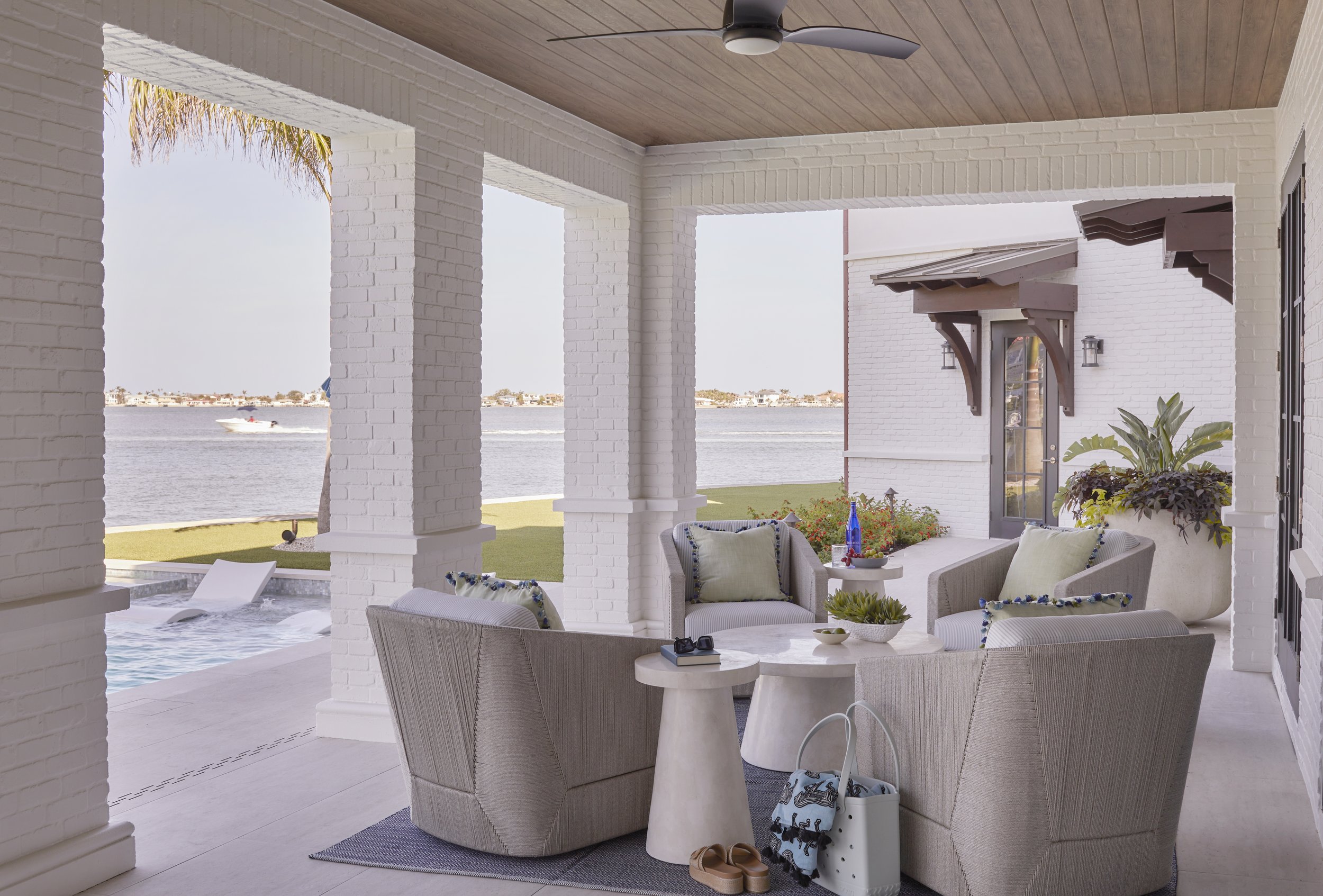 Outdoor covered patio overlooking water with white brick columns, beige patio furniture, and decor.