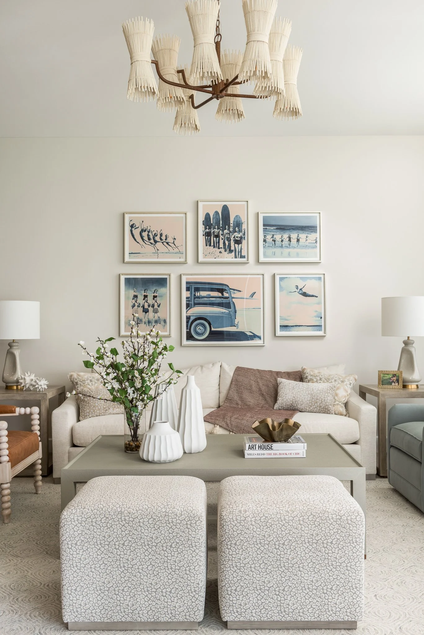 Living room with a coffee table, two ottomans, a sofa, side tables, lamps, wall art, and a chandelier.