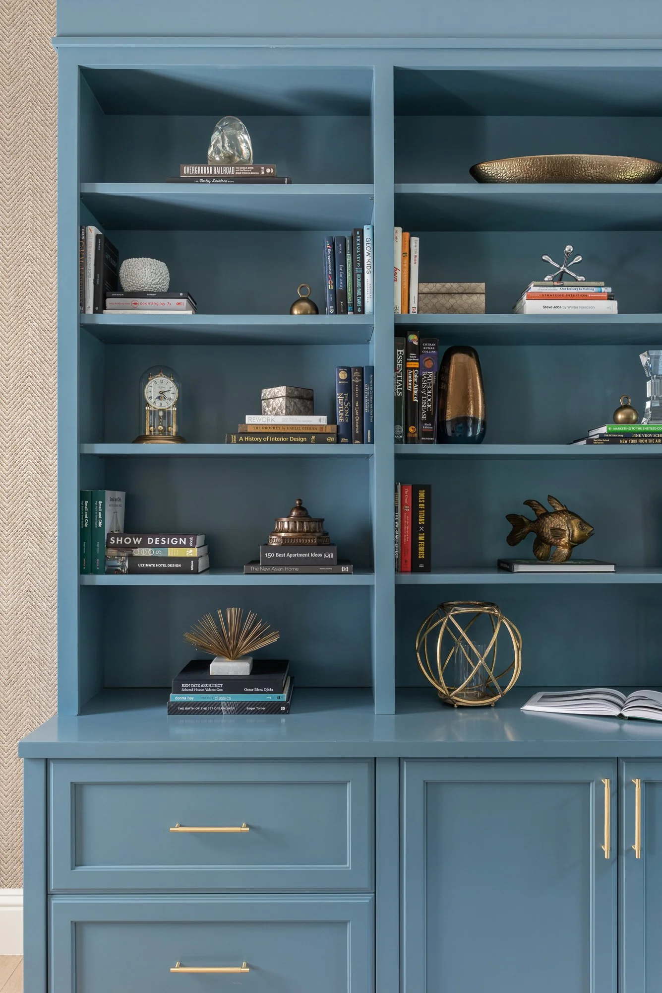 Blue bookshelf with decorative books, sculptures, and ornaments inside and on top.