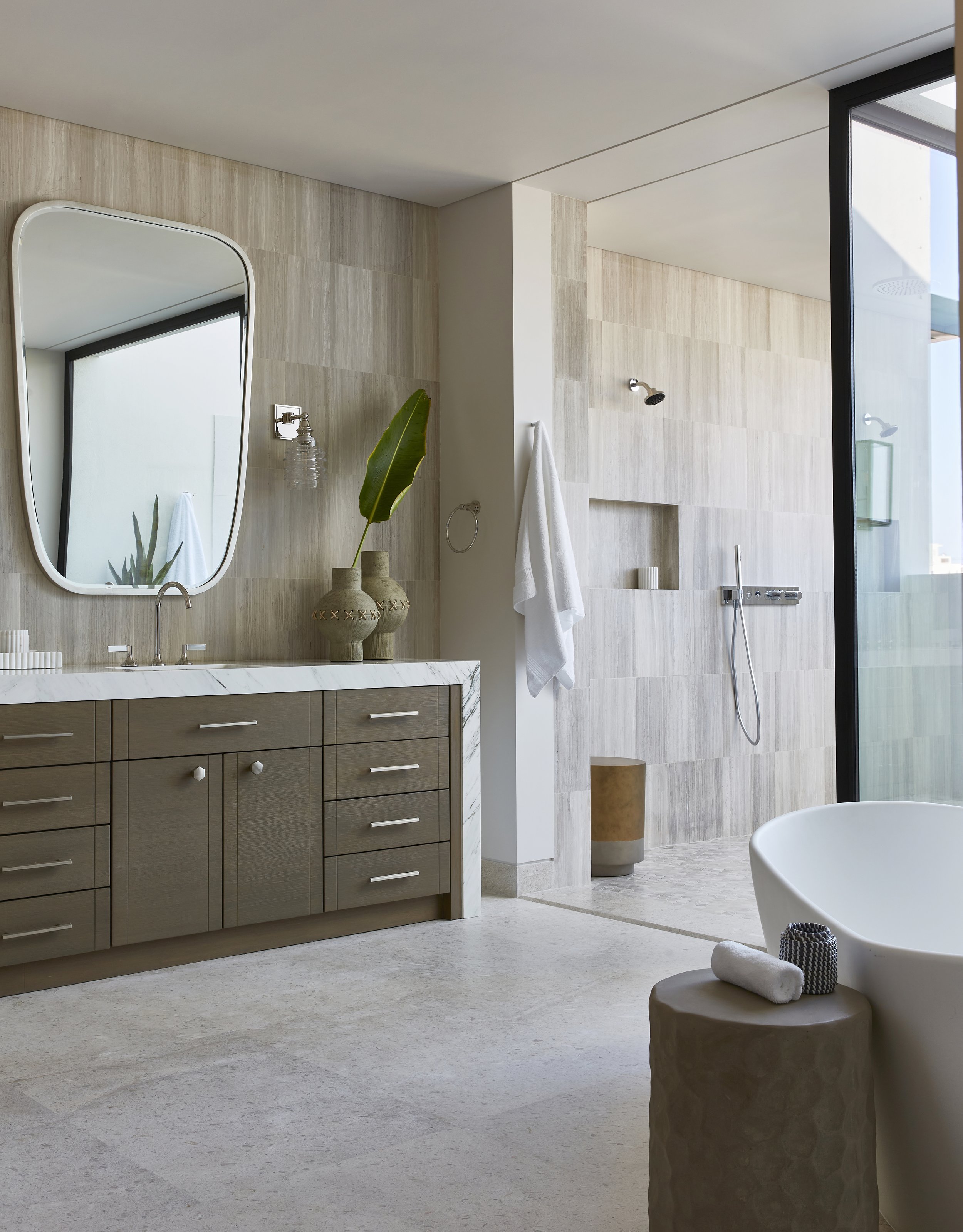 Modern bathroom with a marble vanity, large mirror, potted plant, and a glass-enclosed shower with a rainfall showerhead and a bathtub.