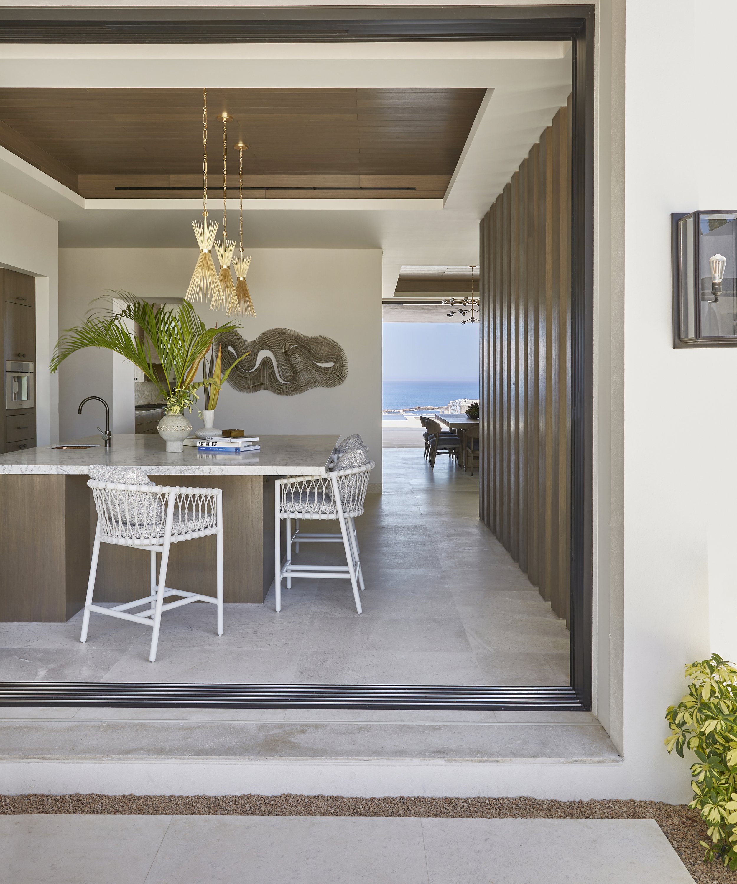 Modern open-concept kitchen and dining area with a view of the ocean in the background, light-colored walls, wooden details, and minimal decor.