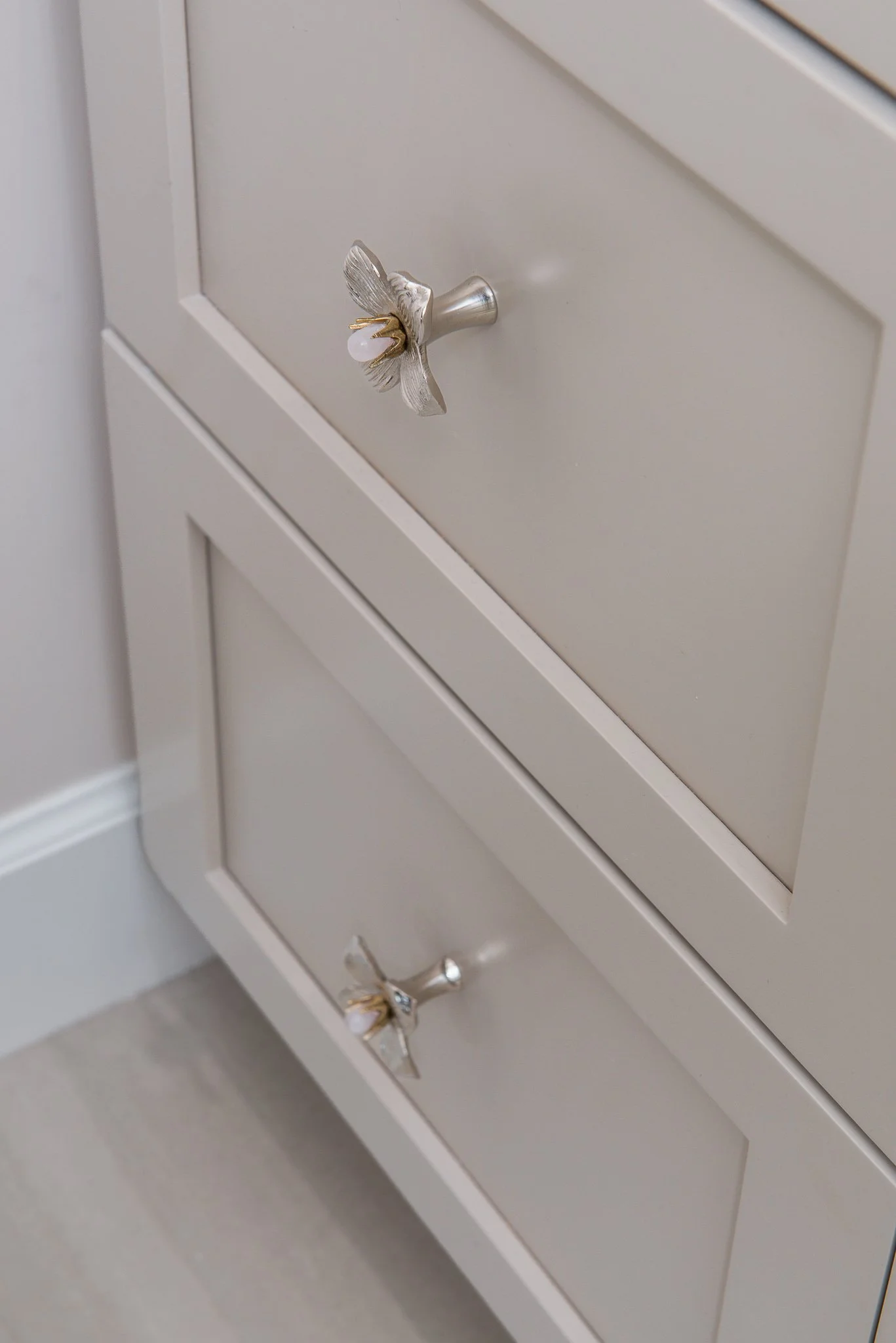 Close-up of a white cabinet with silver butterfly-shaped drawer handles, each with a small pink and clear jewel on top.