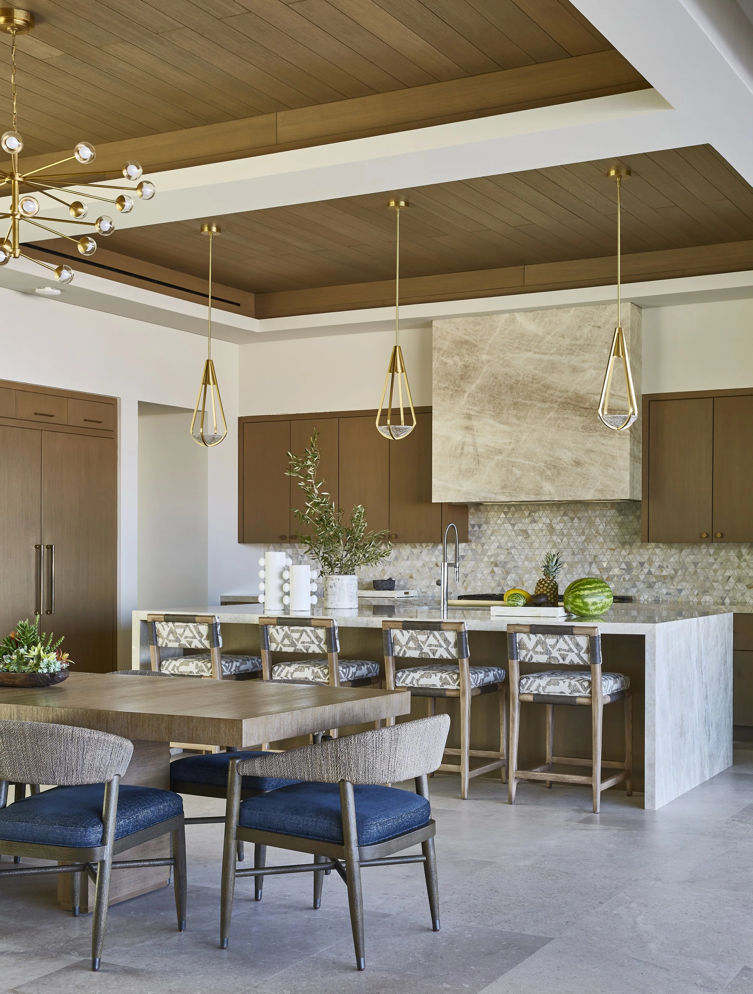 Modern kitchen with wood cabinets, beige marble island, pendant lights, and decorative fruits.