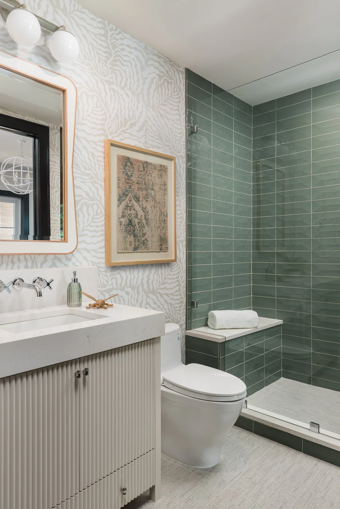 Modern bathroom with a white vanity, wall-mounted mirror, framed artwork, and a clear-glass shower with green tiles.
