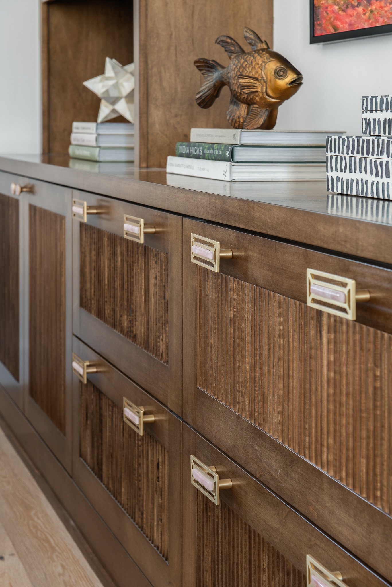 Close-up of a wooden sideboard with gold and pink handles, decorated with books, a gold fish sculpture, and a star-shaped decorative object.