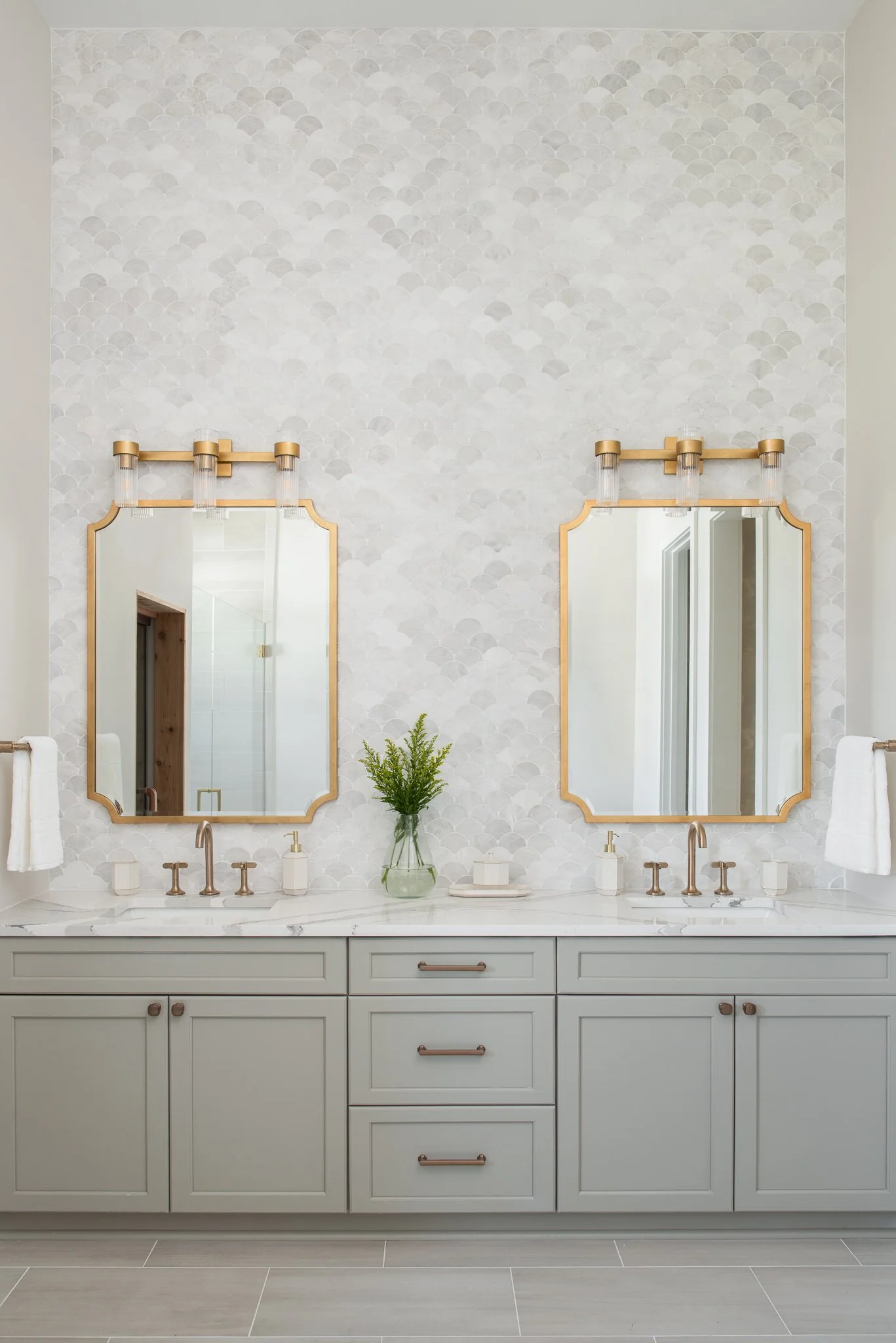 A double vanity bathroom with two mirrors, two faucets, a plant, and white towels, with smoky quartz wall tiles.