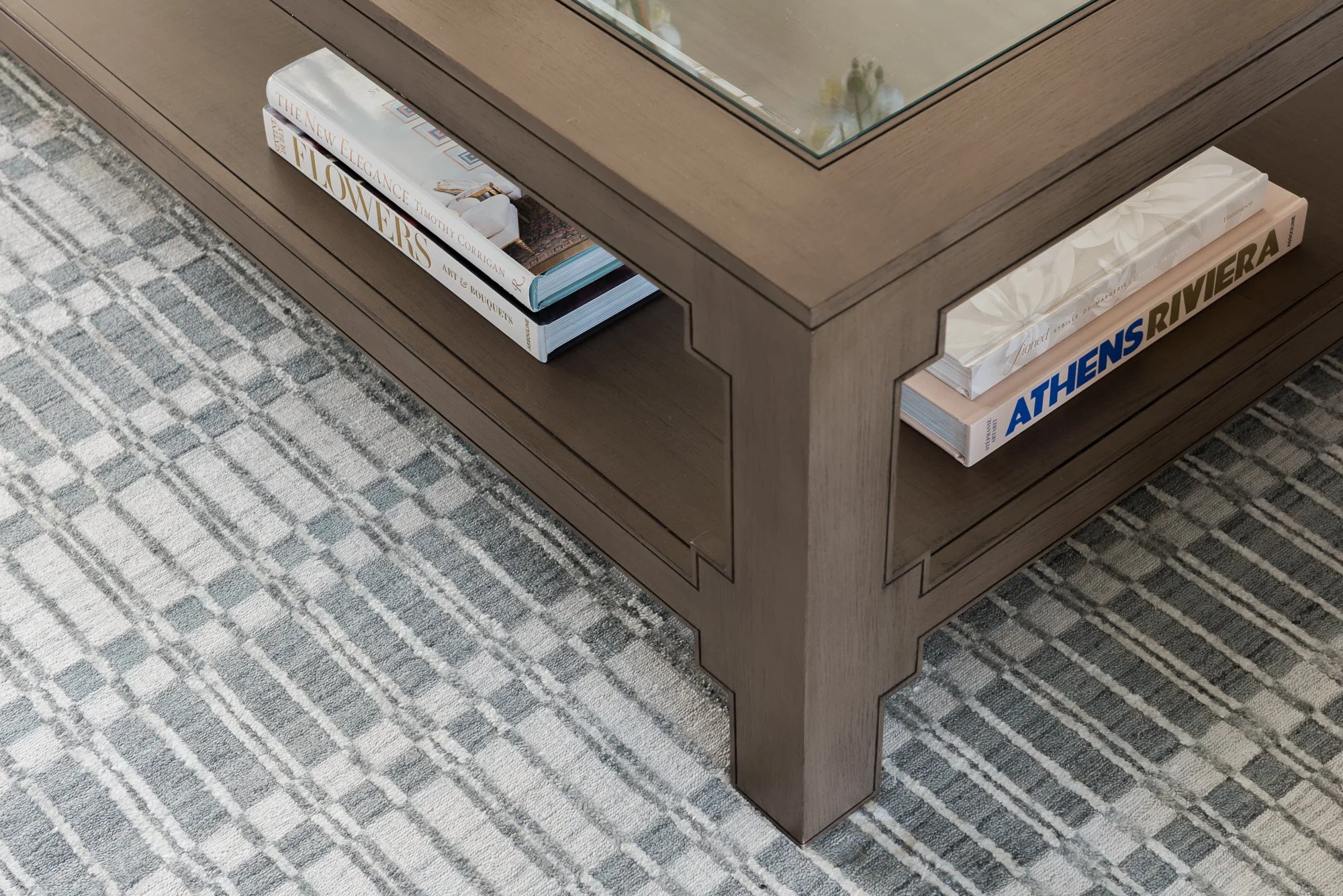 Close-up of a wooden coffee table with books on the lower shelf, placed on a patterned rug.