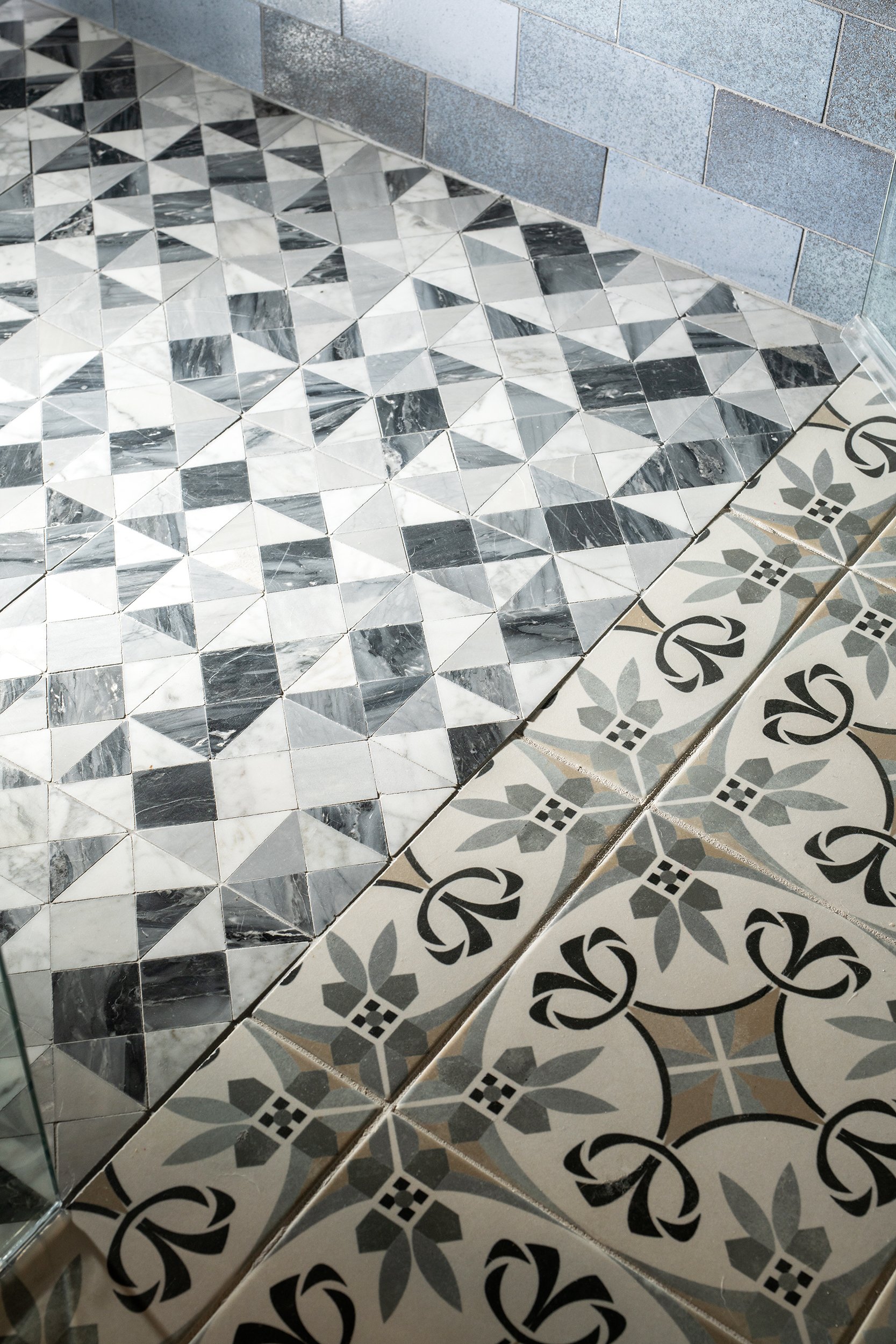 Close-up of patterned black and white marble and decorative tiles on a floor near a gray brick wall.