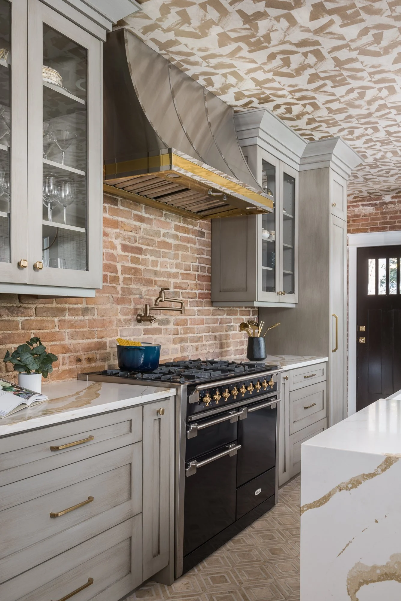 A modern kitchen with light wood cabinets, a black stove, and a brick wall backsplash.