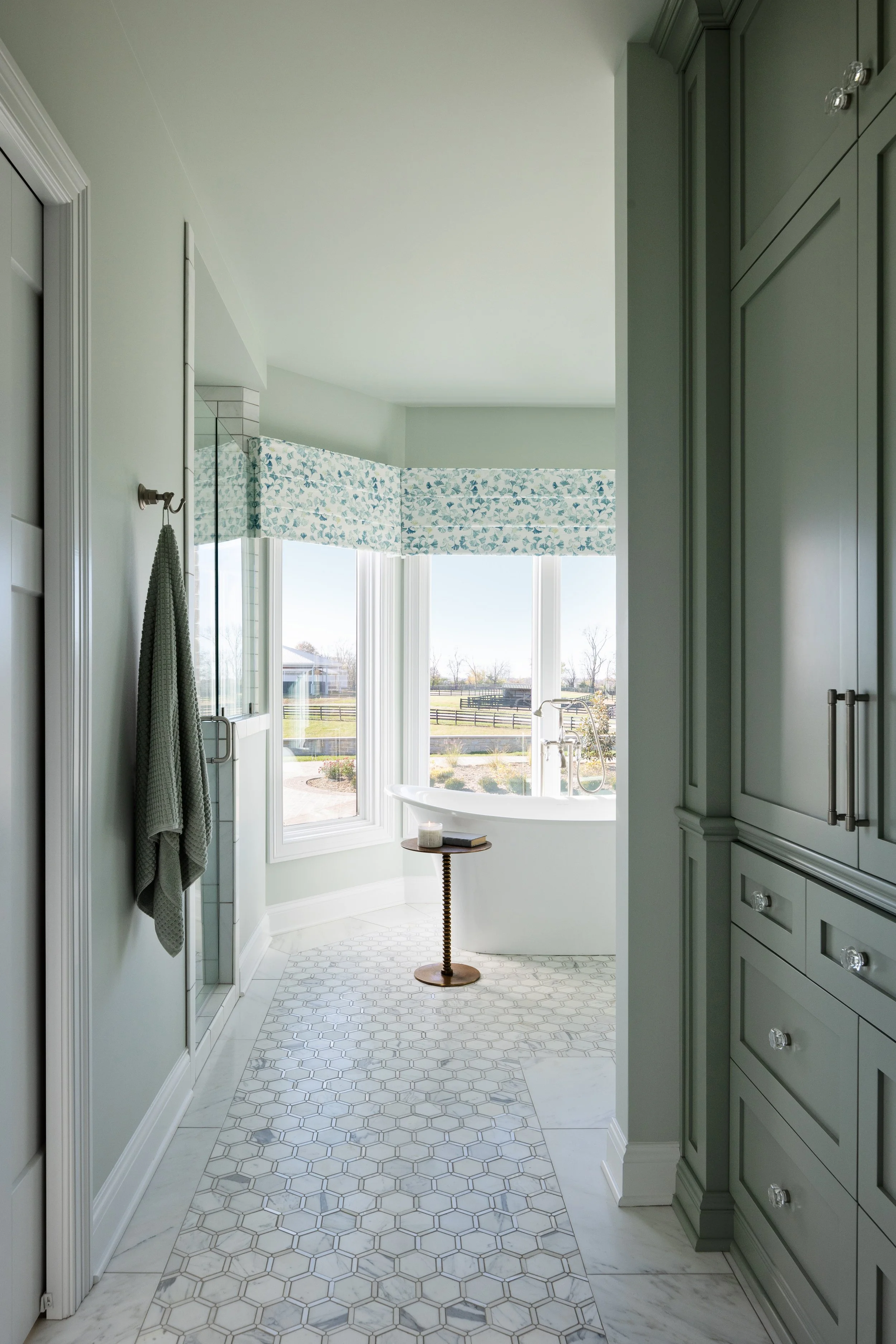 Bathroom with a large window, bathtub, green cabinetry, and hexagonal tile floor.
