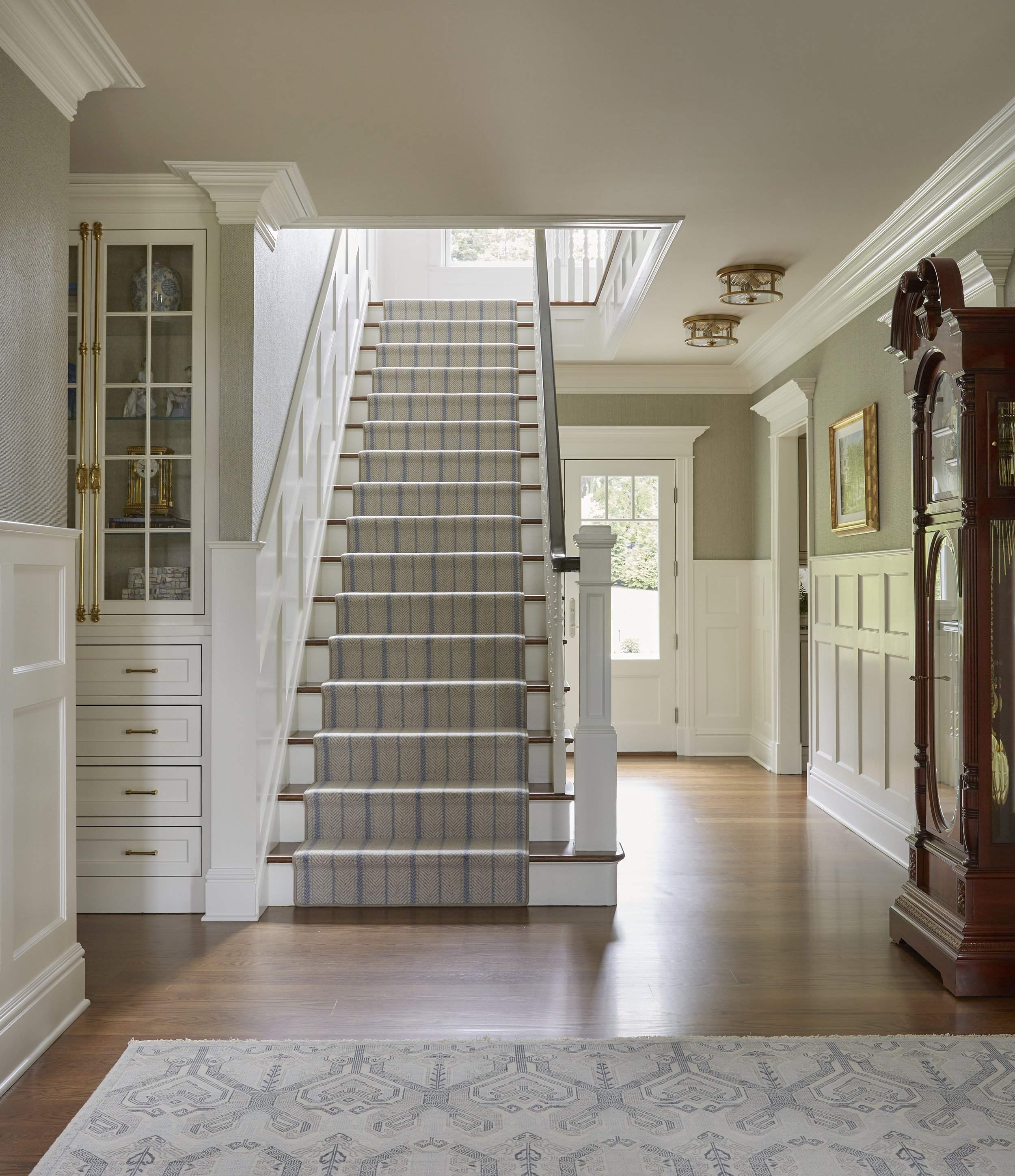 Interior view of a home foyer with a staircase, wooden flooring, and decorative wall and ceiling moldings.