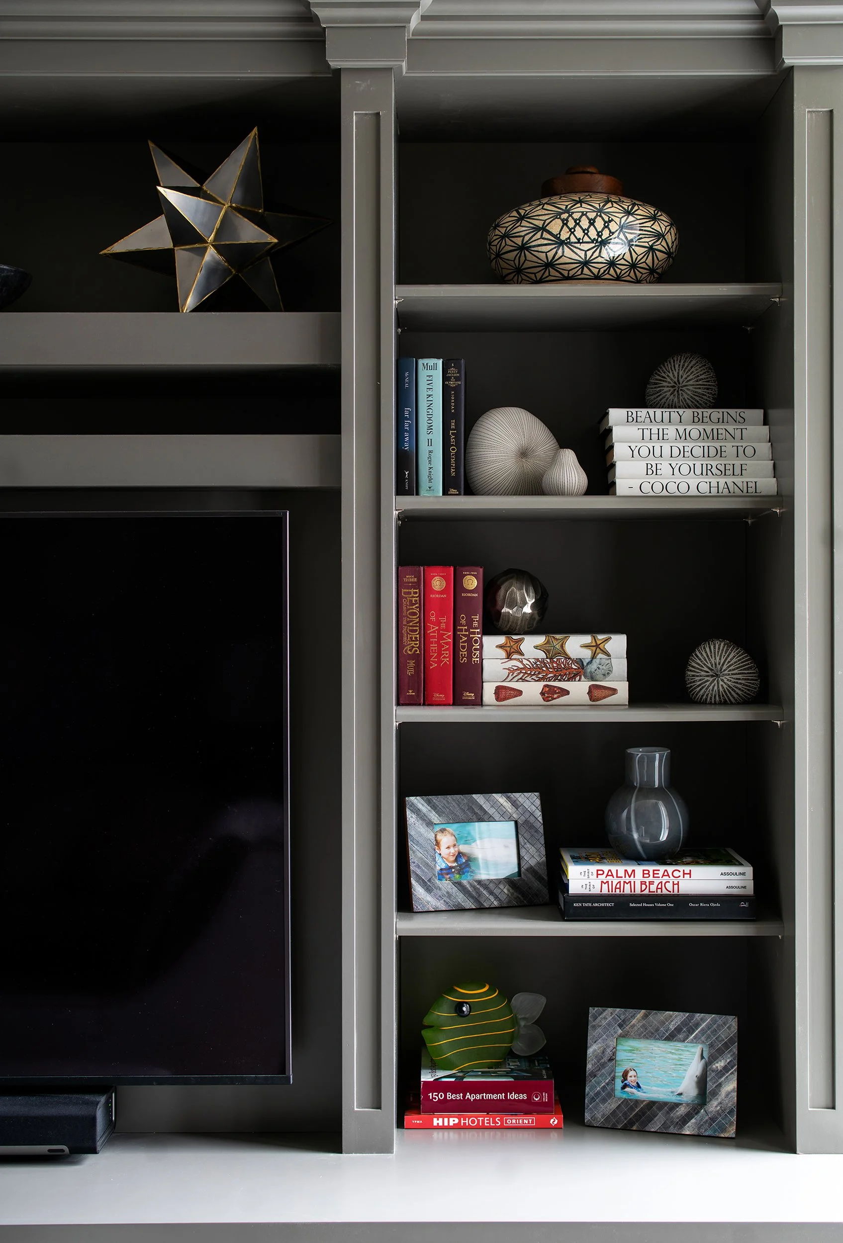Gray bookshelf with decorative items, books, and framed photos