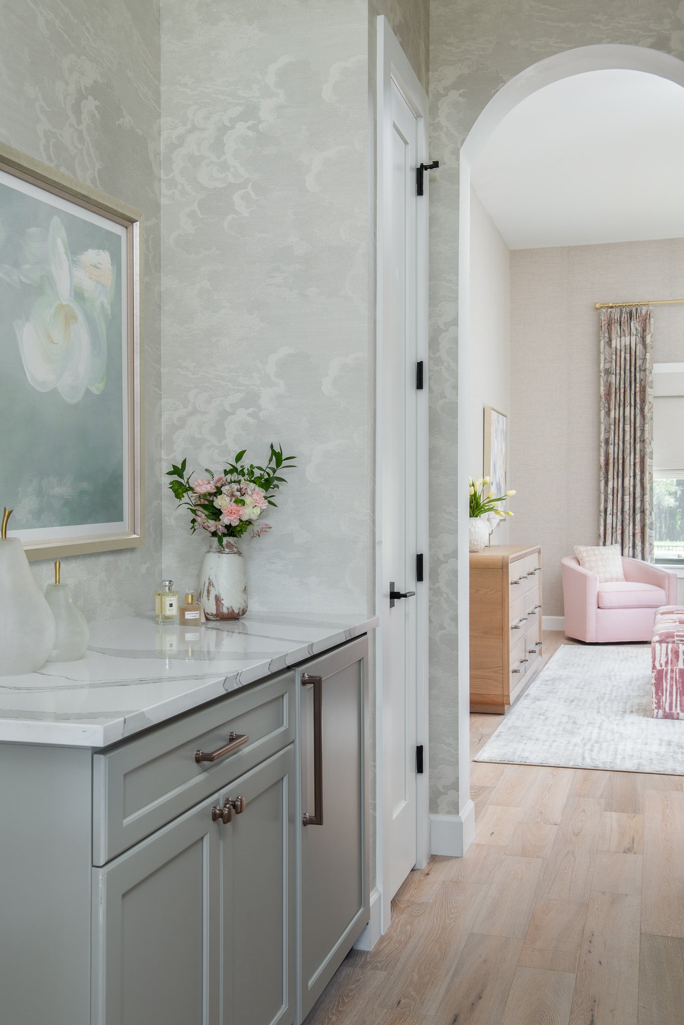A hallway leading into a living room with pink furniture, floral curtains, and a window.