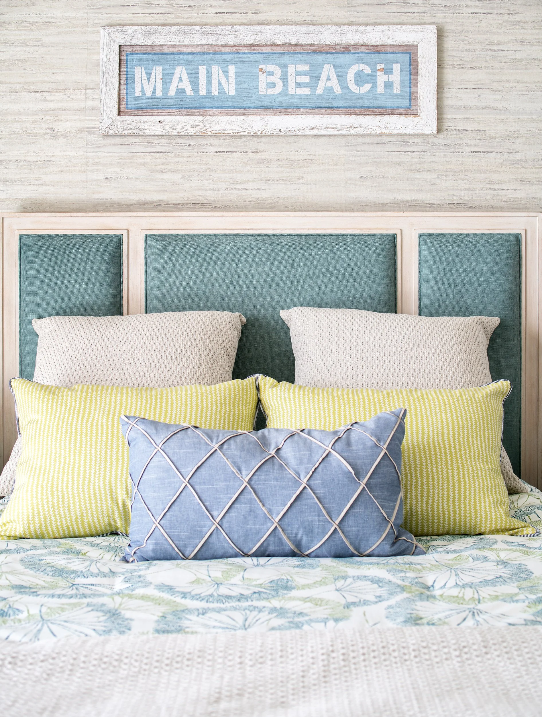 Beach-themed bedroom with a light blue headboard, patterned pillows, and a "Main Beach" sign on the wall.