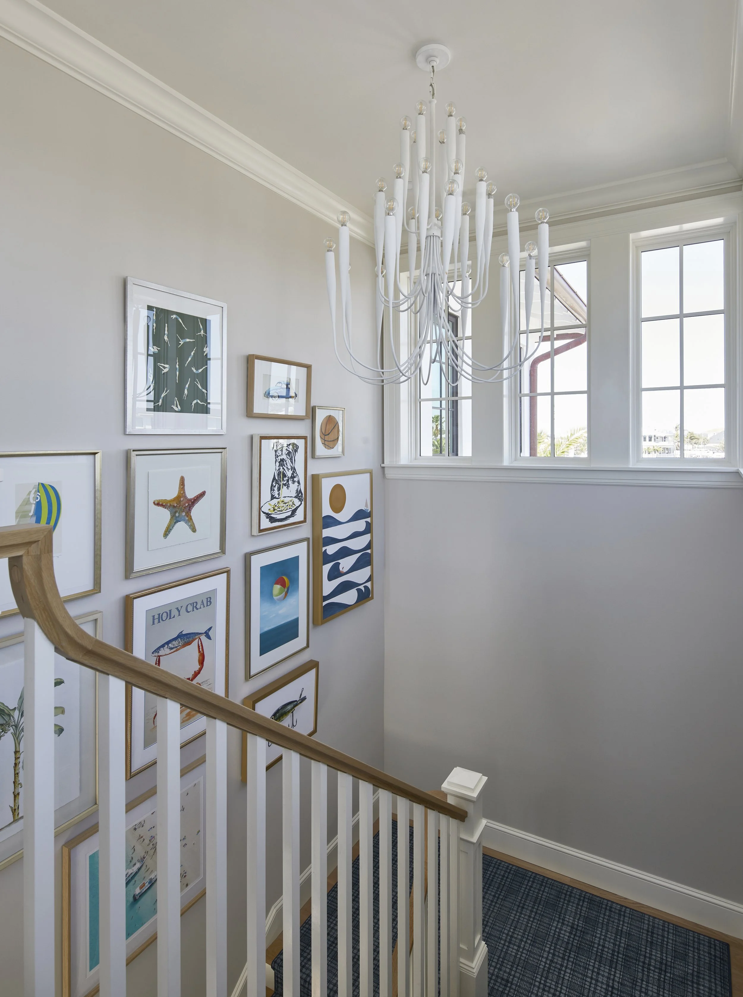 A staircase landing with wall art, a white chandelier, large windows, and carpeted stairs.