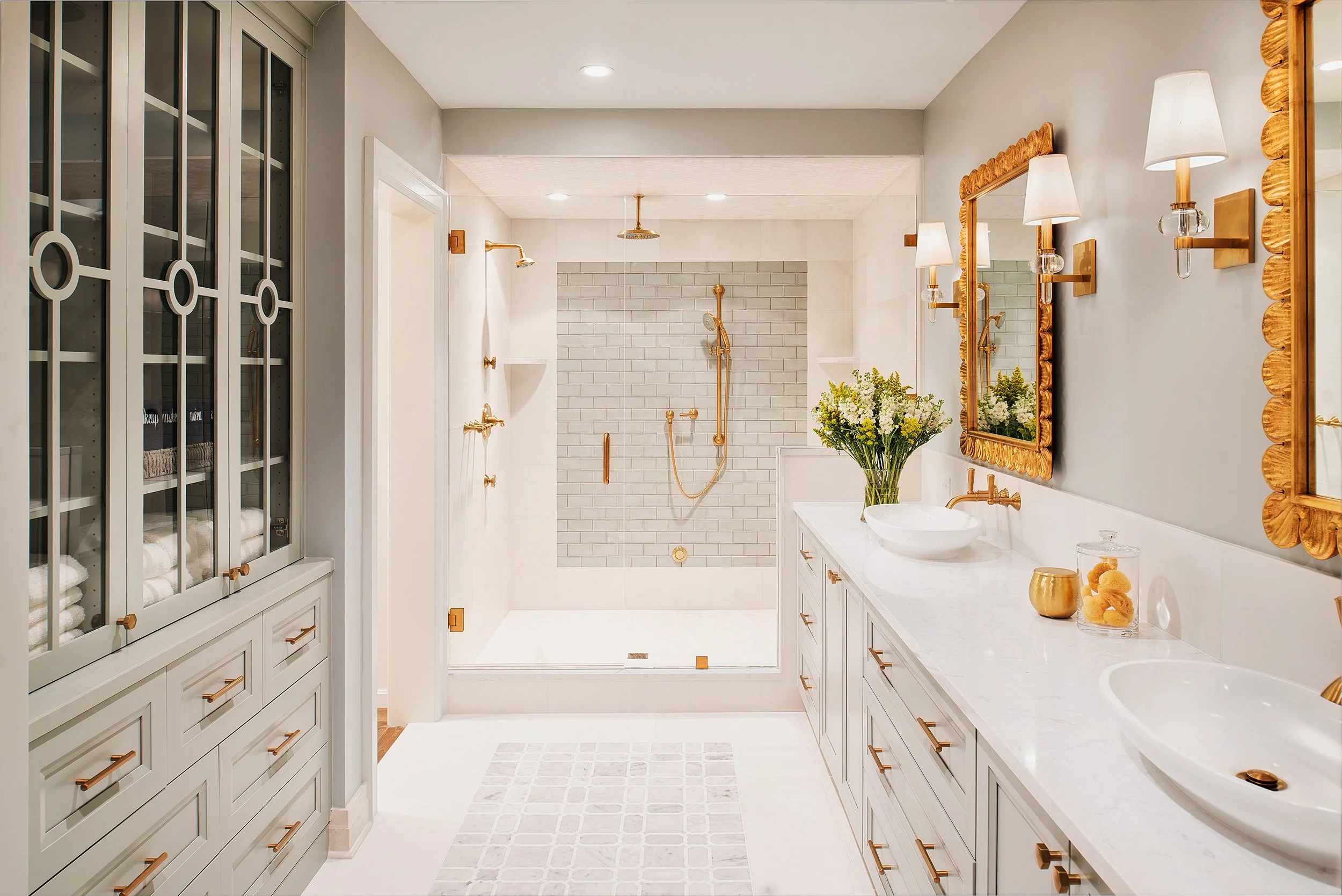 Luxury bathroom with double vanity, gold fixtures, large mirrors, shower with gold accents, and decorative items