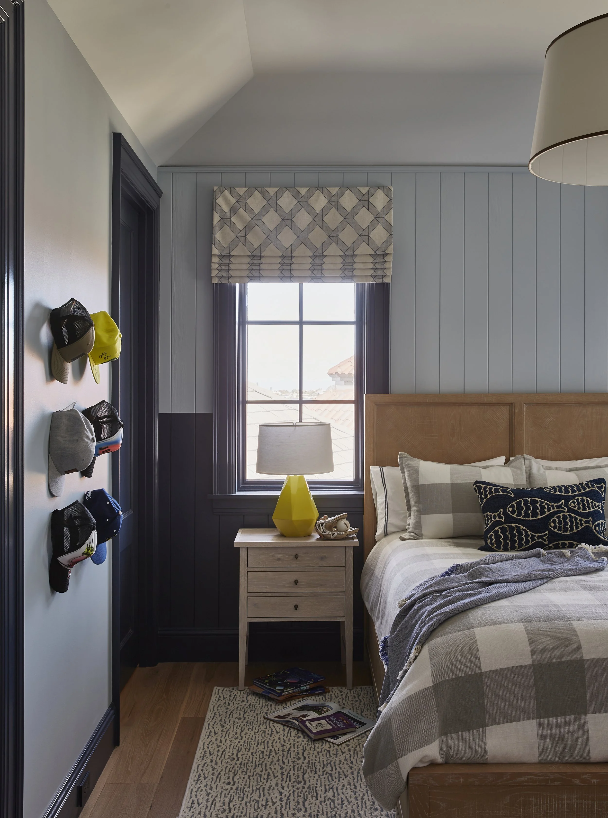 A bedroom with a bed, nightstand, window, and hats on the wall.