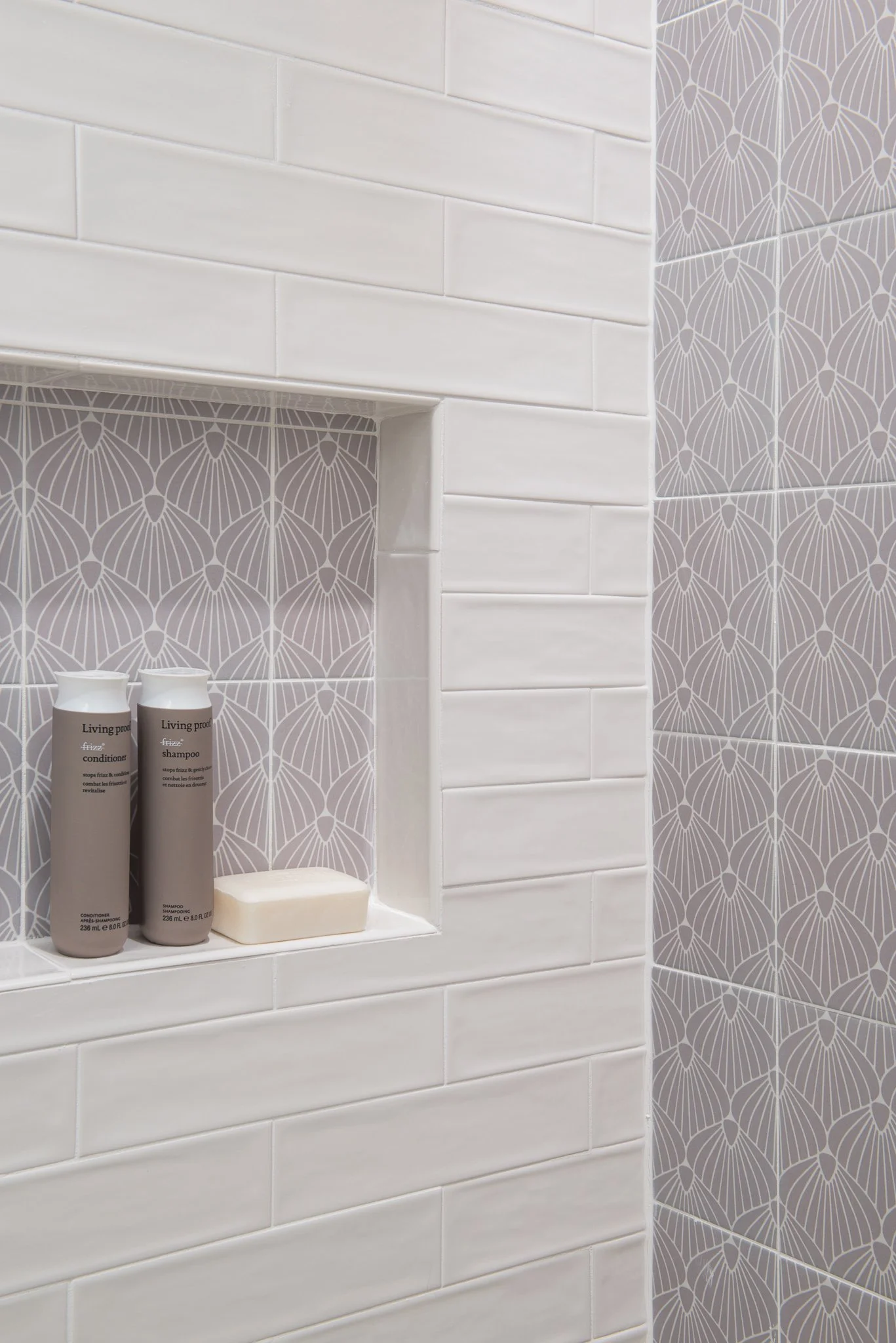 Shower niche with two bottles of shampoo and conditioner, soap, and a decorative patterned tile background.