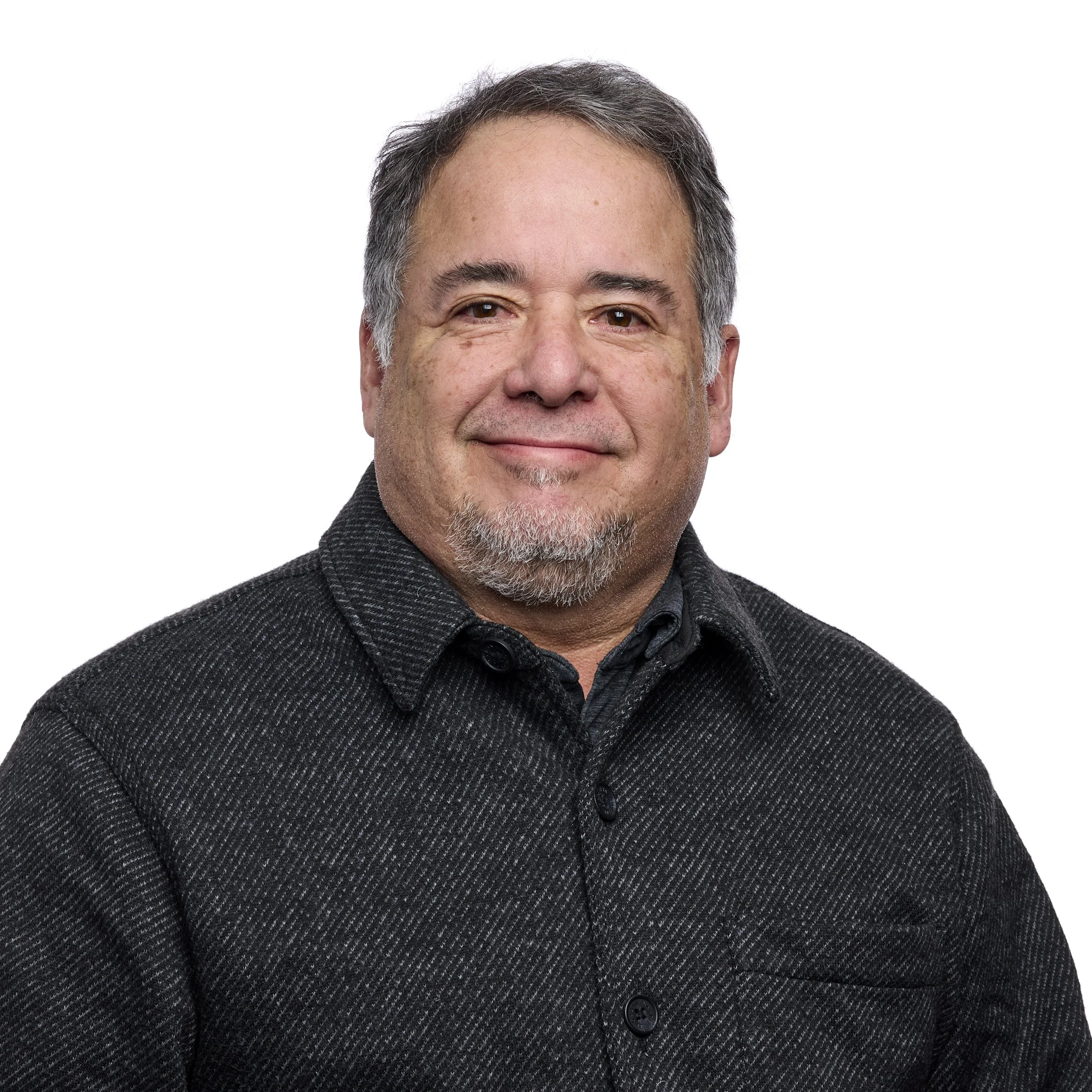 Portrait of a middle-aged man with gray hair, facial hair, wearing a dark textured shirt, smiling against a white background.