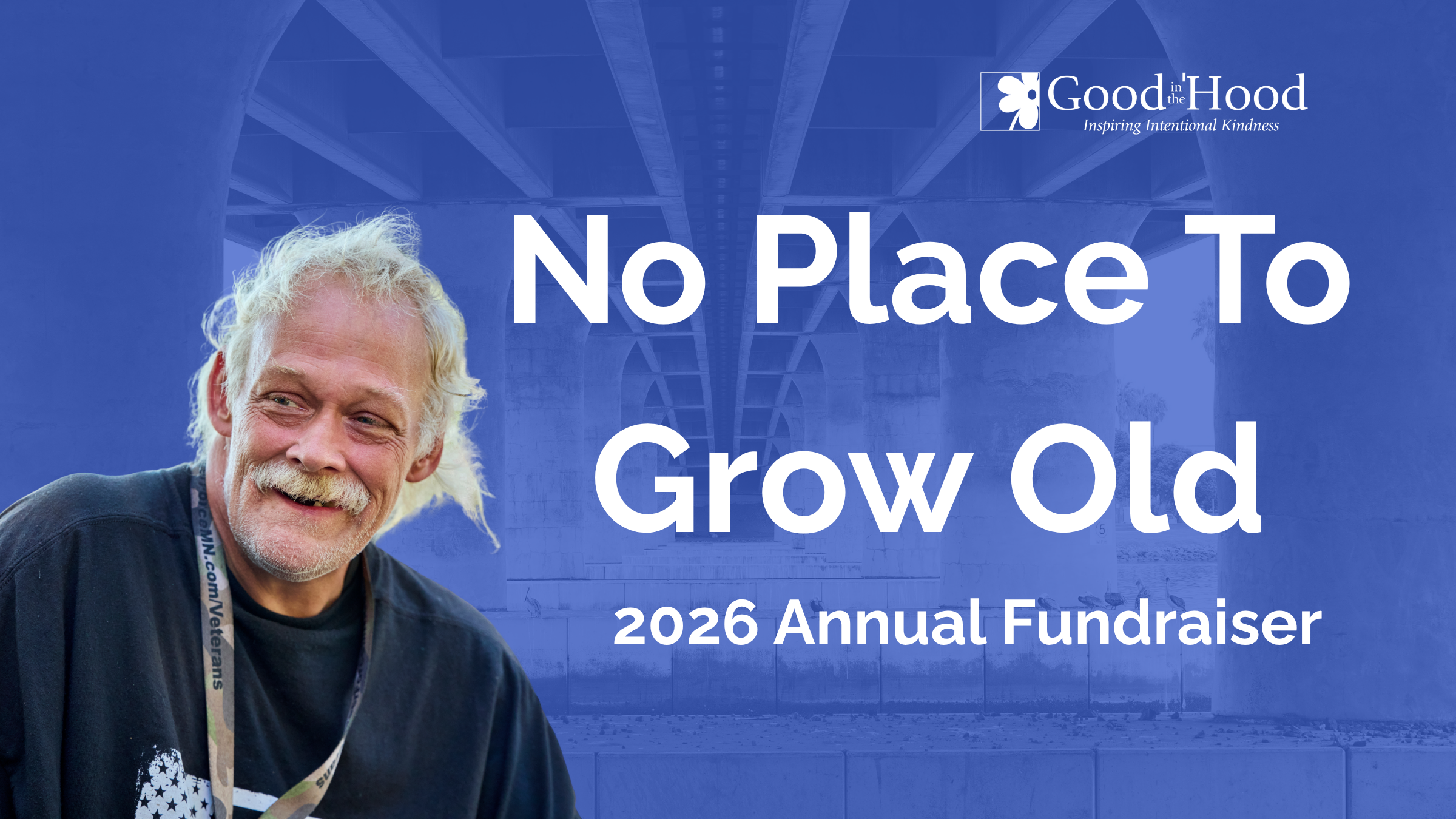 A smiling older man with white hair and a beard, wearing a black jacket and a lanyard, standing outdoors under a bridge. Overlaid on the image is text that reads 'No Place To Grow Old', along with details of a 2026 annual fundraiser by Good in the Hood.