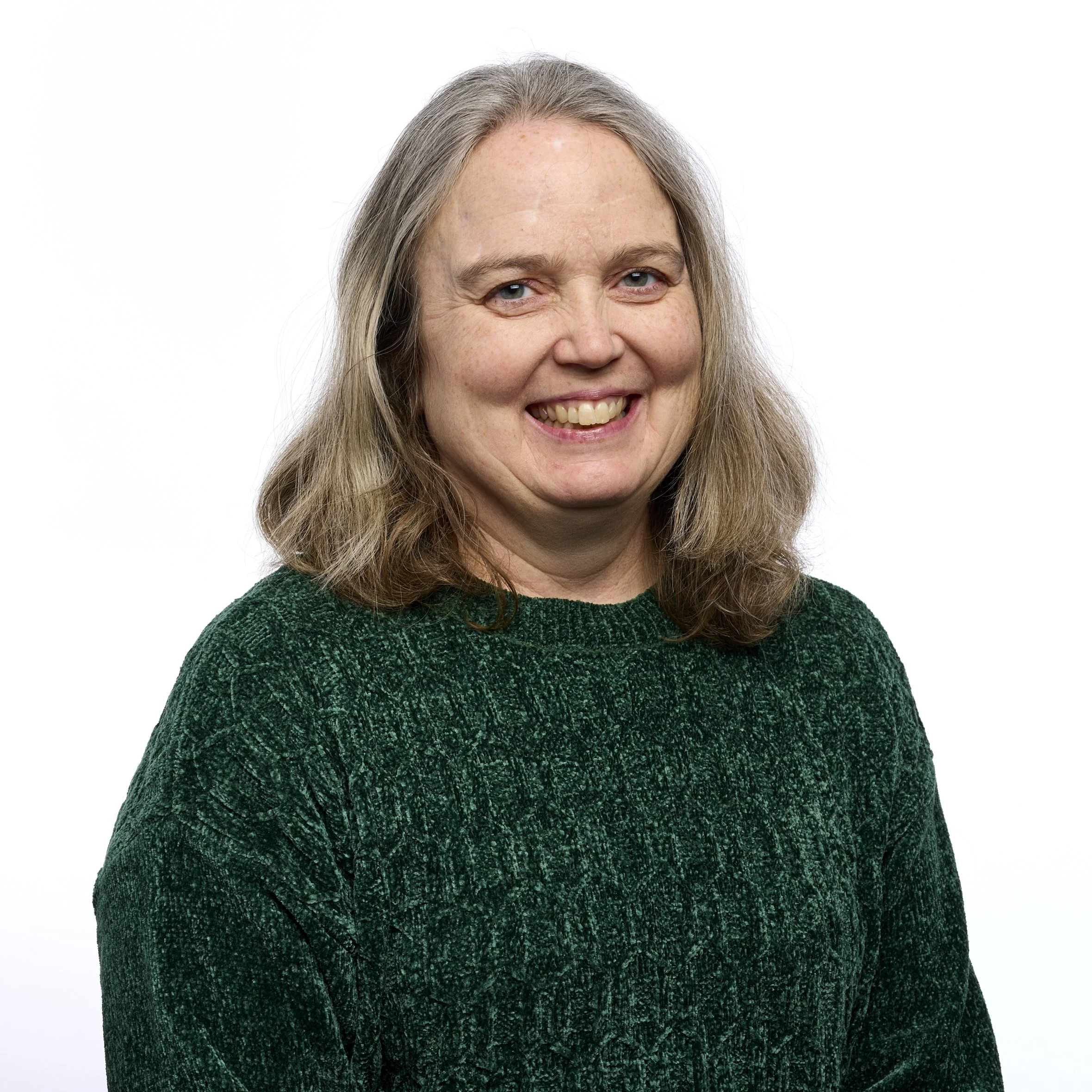 A smiling woman with shoulder-length gray hair, wearing a dark green textured sweater, against a plain white background.