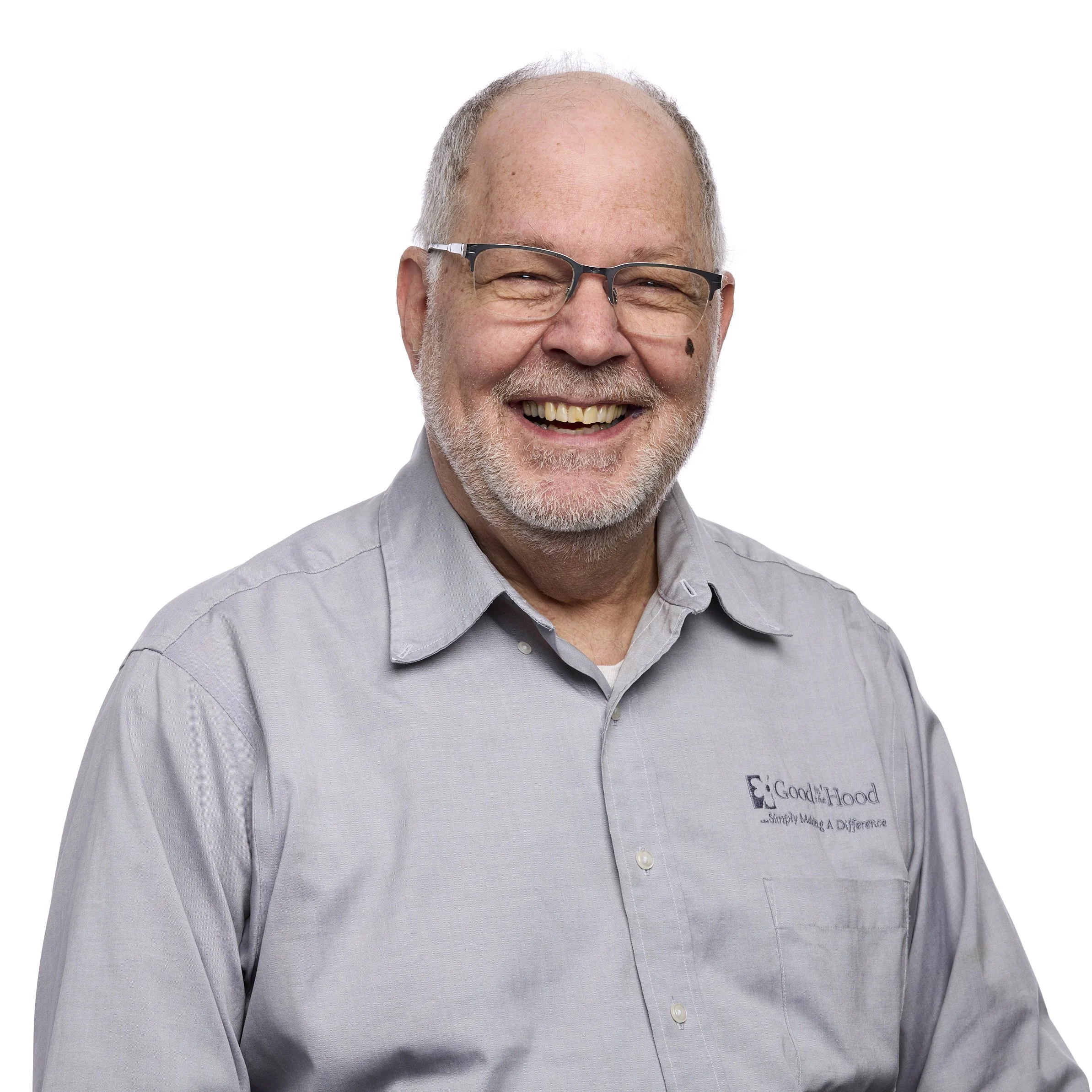 Headshot of an elderly man with glasses and a white beard, smiling against a white background, wearing a light gray button-up shirt with a logo.