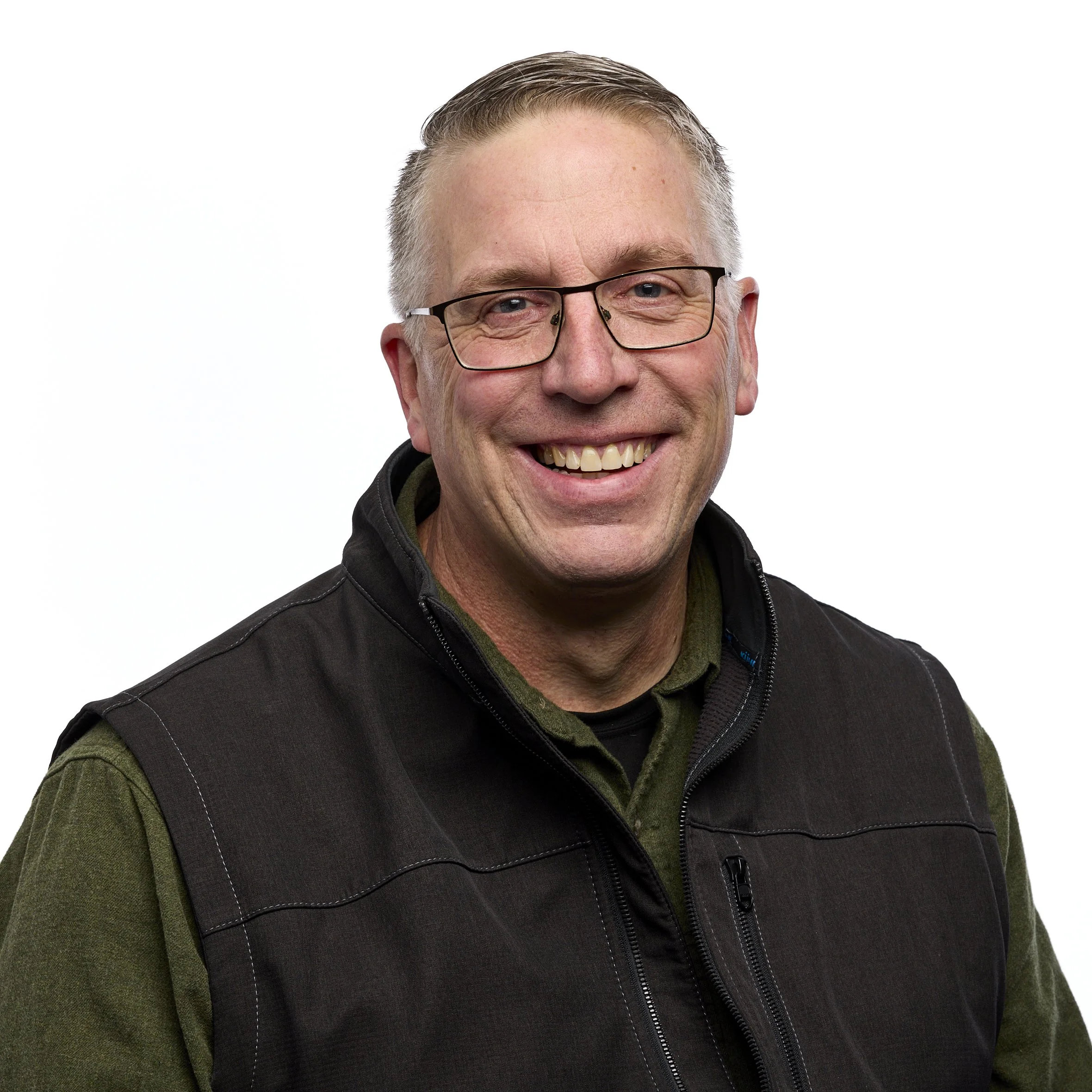 A smiling middle-aged man wearing glasses, a black vest, and a green shirt against a white background.