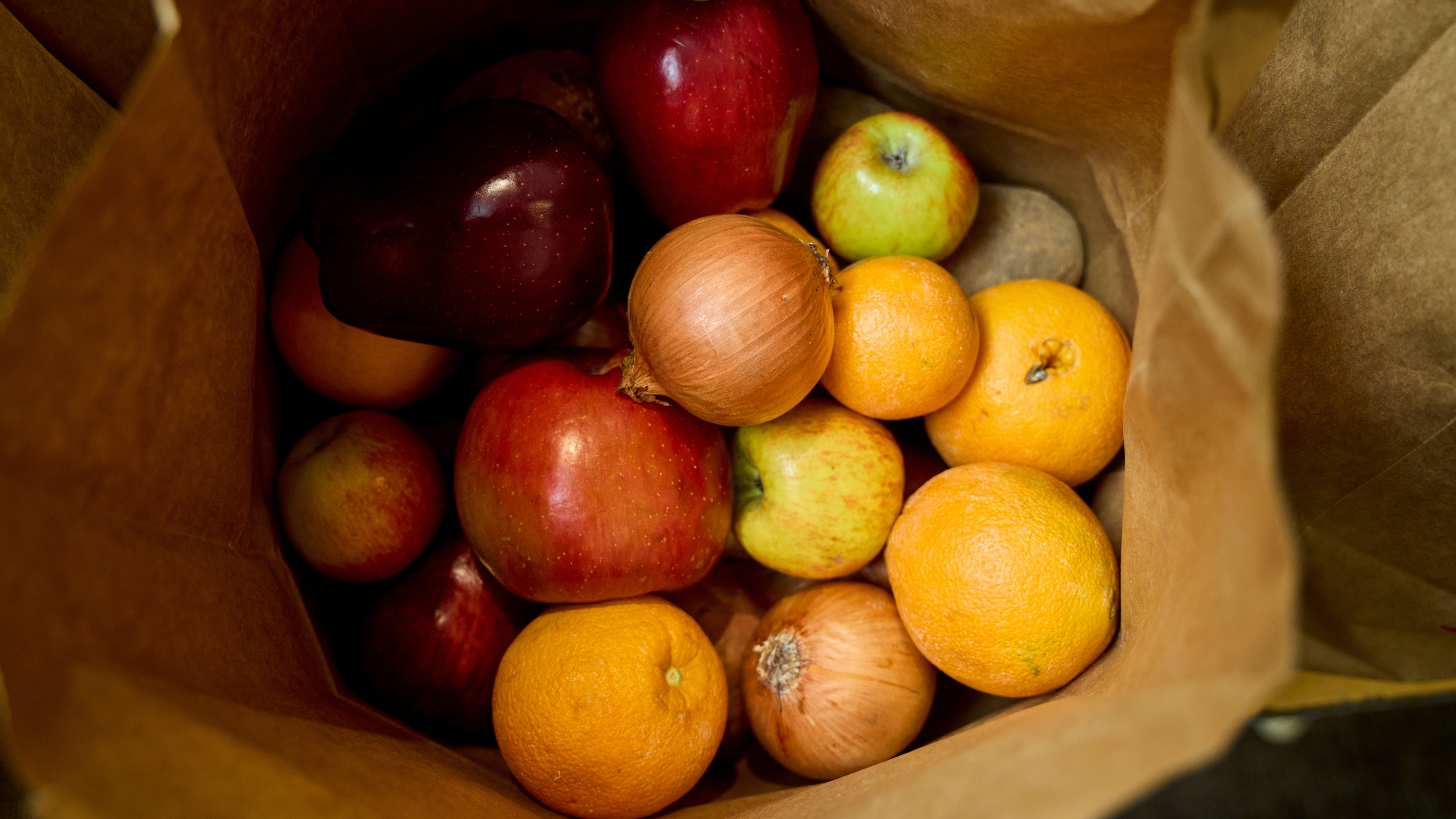 A paper grocery bag filled with apples, oranges, a lemon, and a onion.