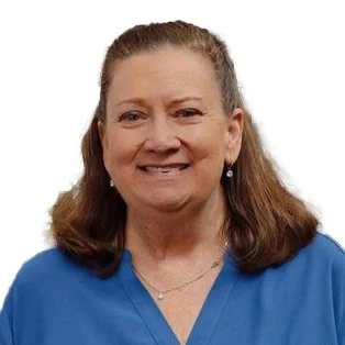 A woman with brown hair wearing a blue top, smiling, and against a plain white background.