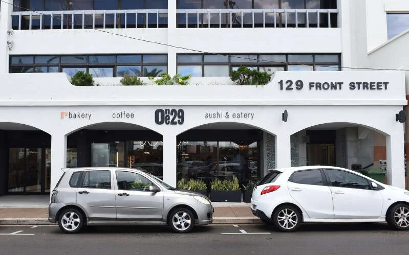Exterior of a building with signs for a bakery, coffee shop, sushi, and eatery with parked cars in front and the address 129 Front Street.