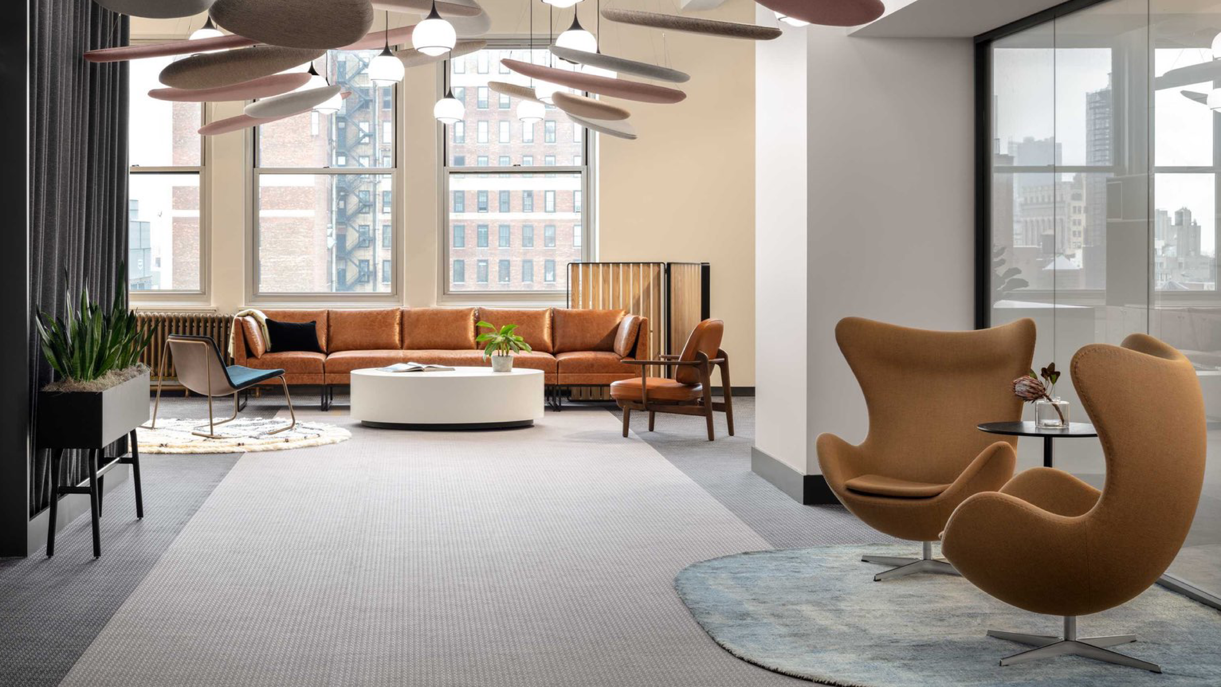 Modern living room with large windows, tan seating, a white round coffee table, and a variety of chairs and decor.