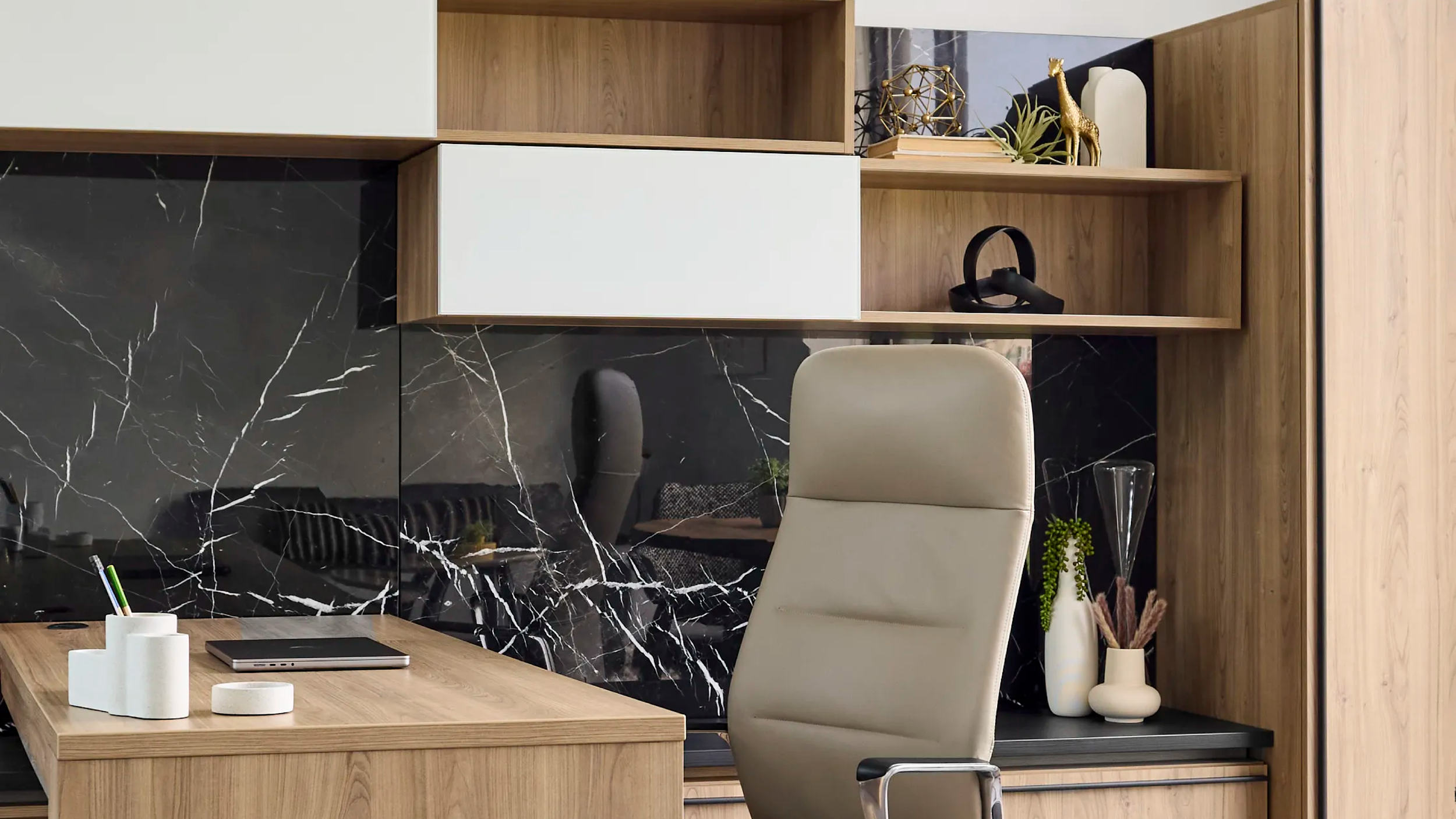 Office desk with beige chair, black marble wall, and wooden shelving with decorative plants and sculptures.