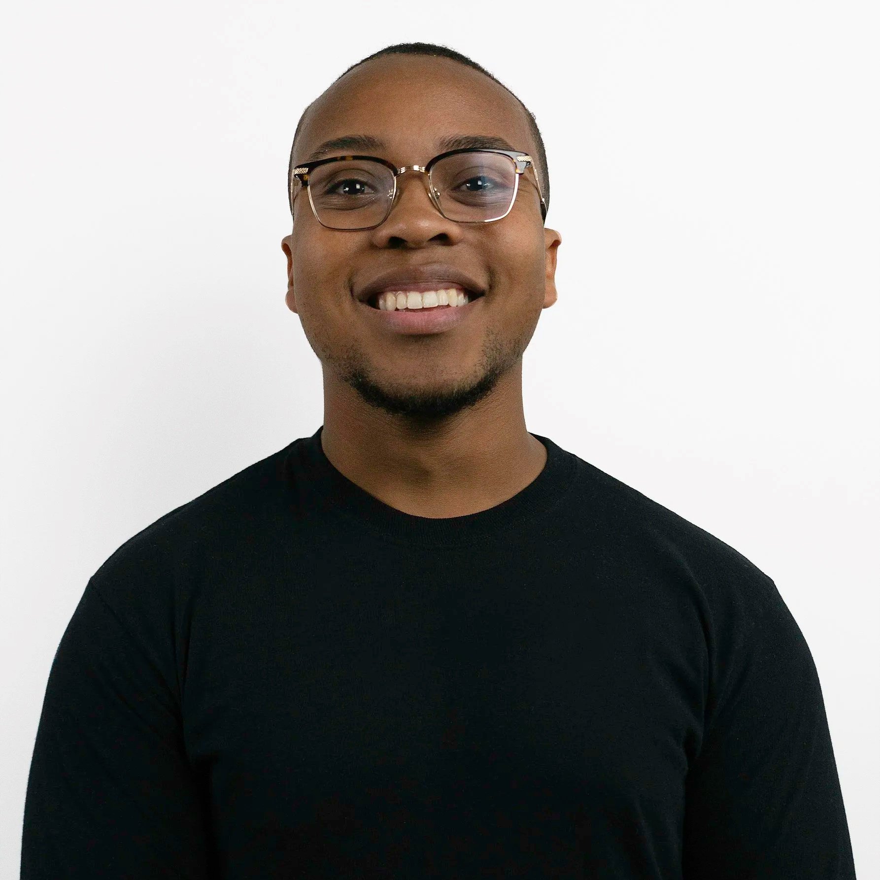Portrait of a smiling young African American man wearing glasses and a black shirt against a white background.