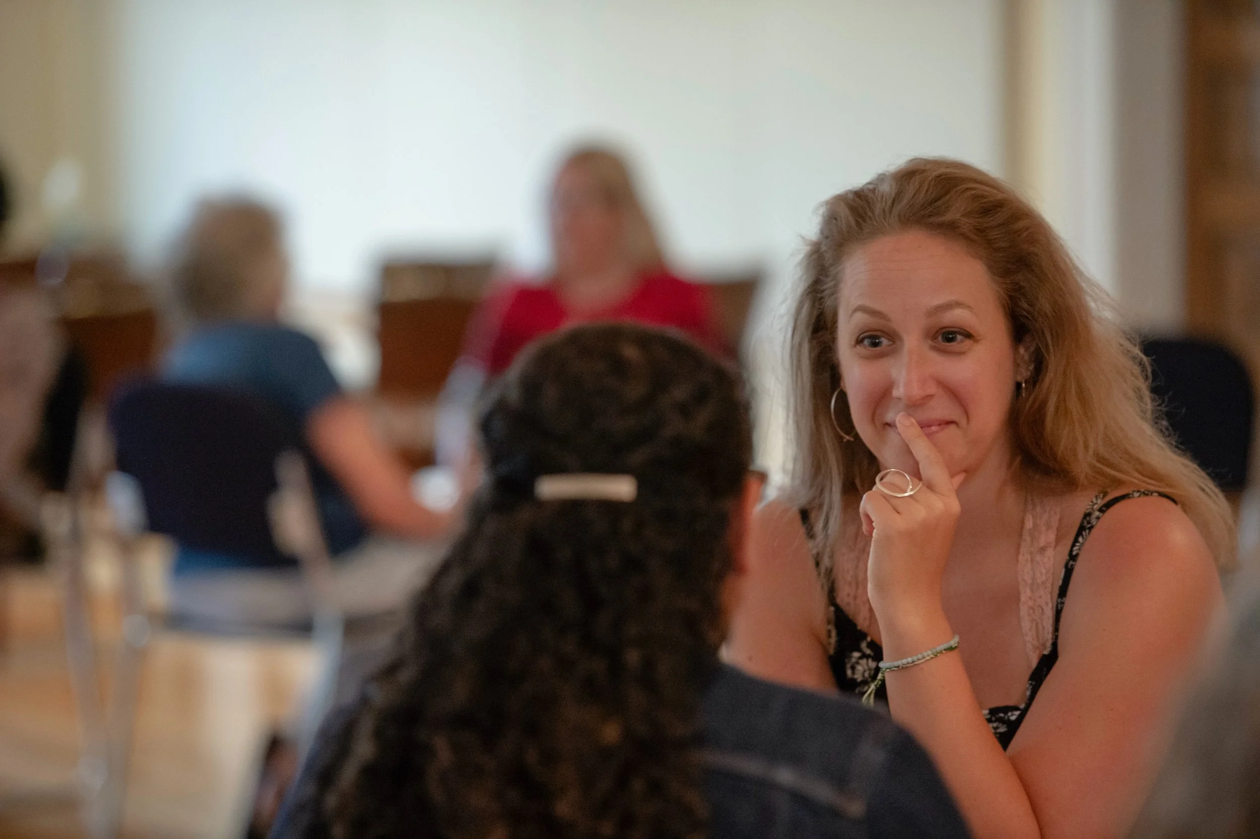 Annabeth Novitzki smiling with a finger to her lips, listening to someone across from her at a workshop