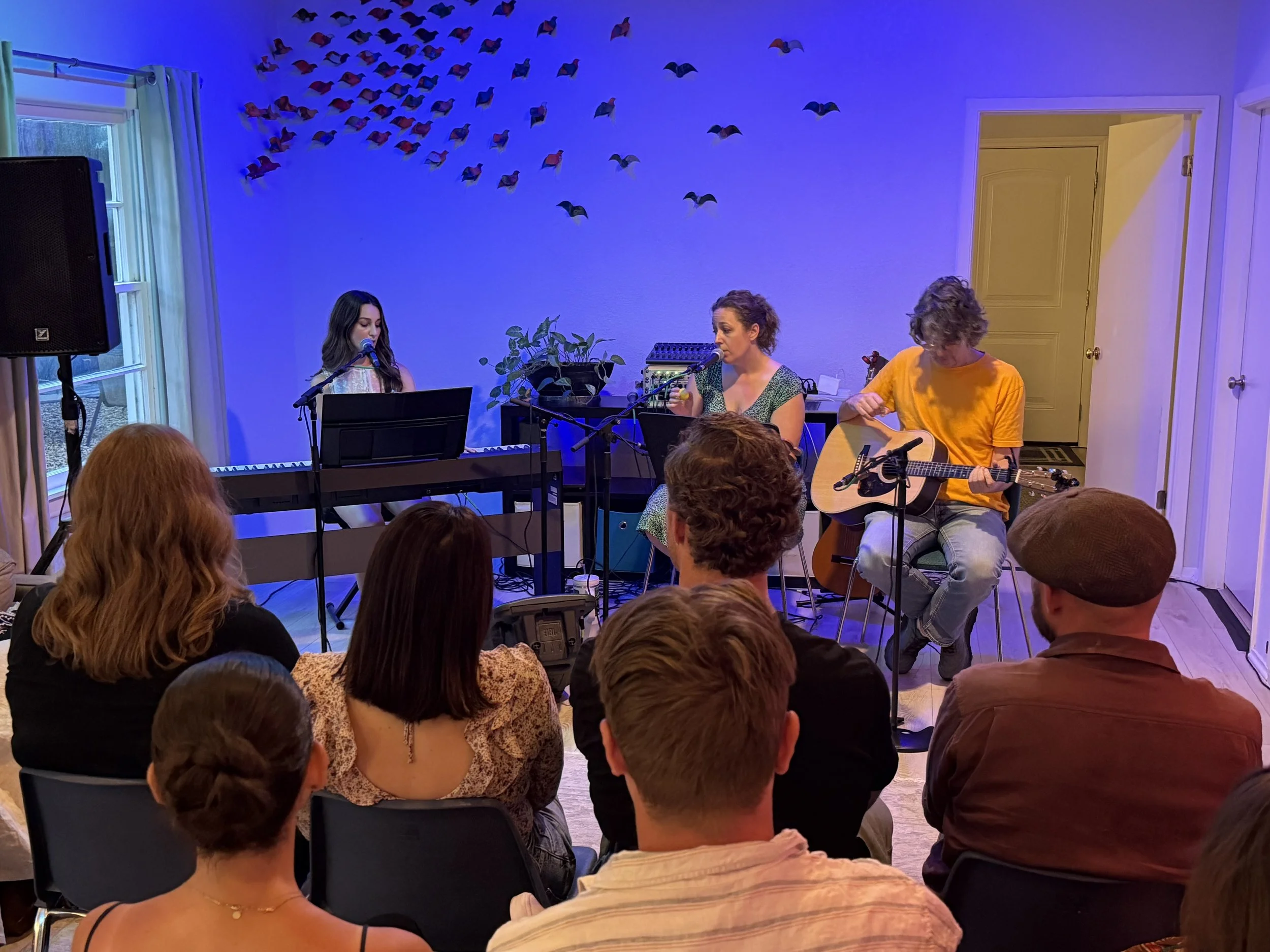 Annabeth singing with two of her students, one at the keyboard and one on guitar, in front of a small audience in her Austin studio