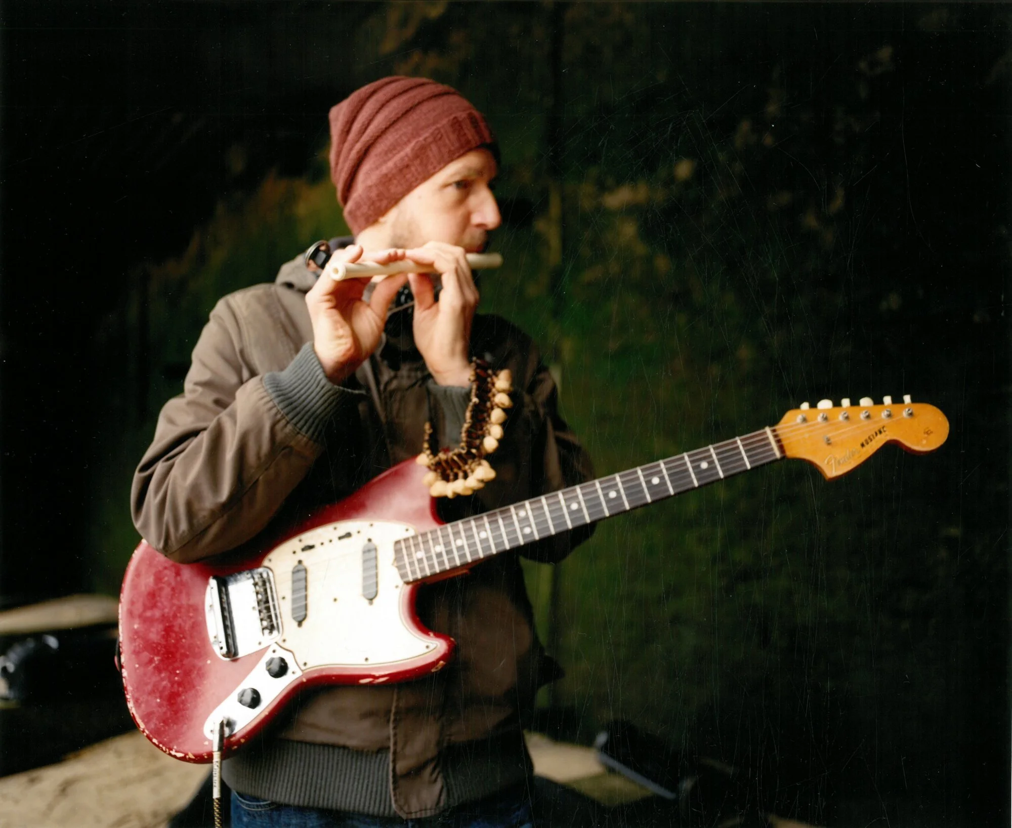 Wilson Novitzki playing a wooden flute, with a red electric guitar slung across him