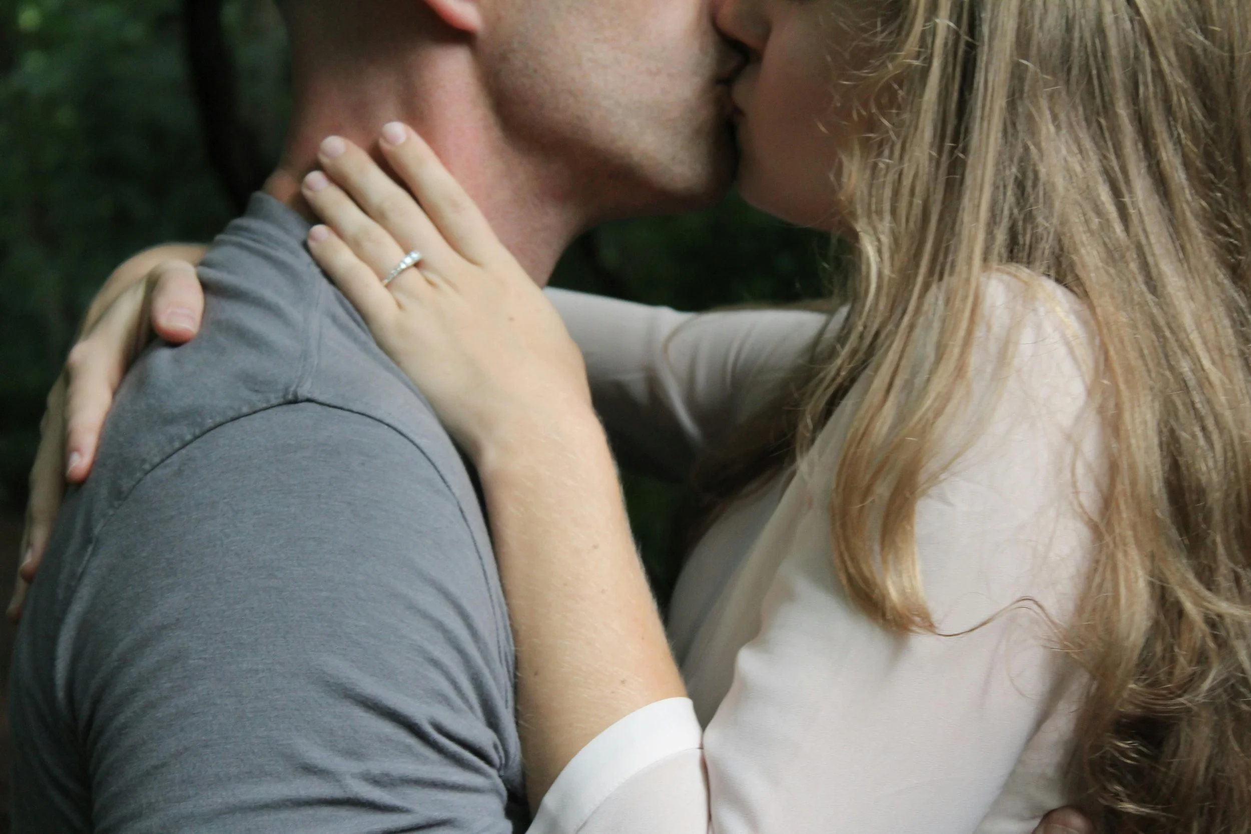 A couple kissing, with the woman holding the man's face and wearing a wedding ring.