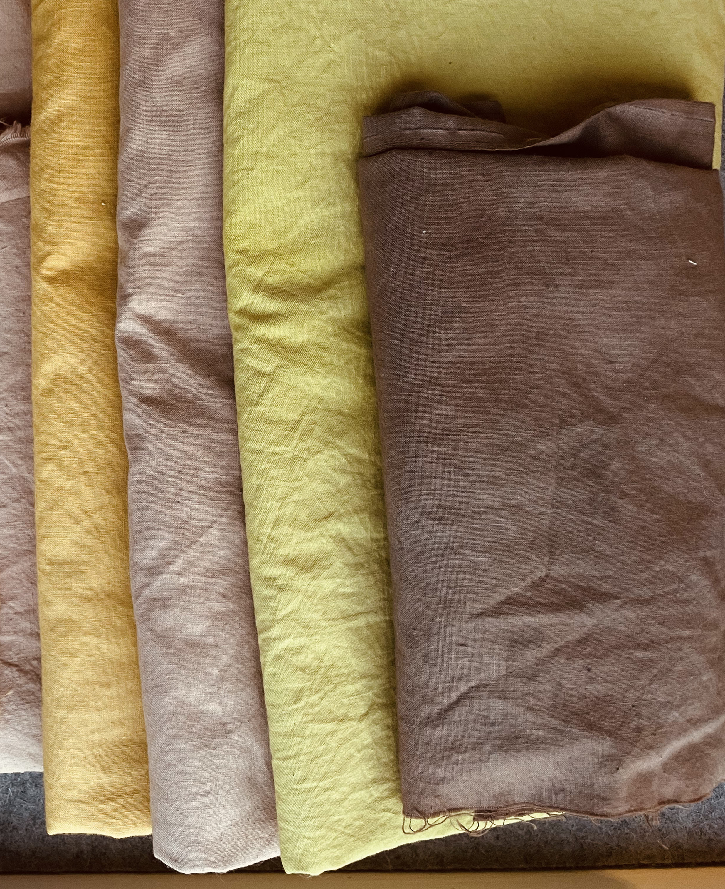 Four rolls of fabric in yellow, taupe, green, and brown colors, arranged side by side.