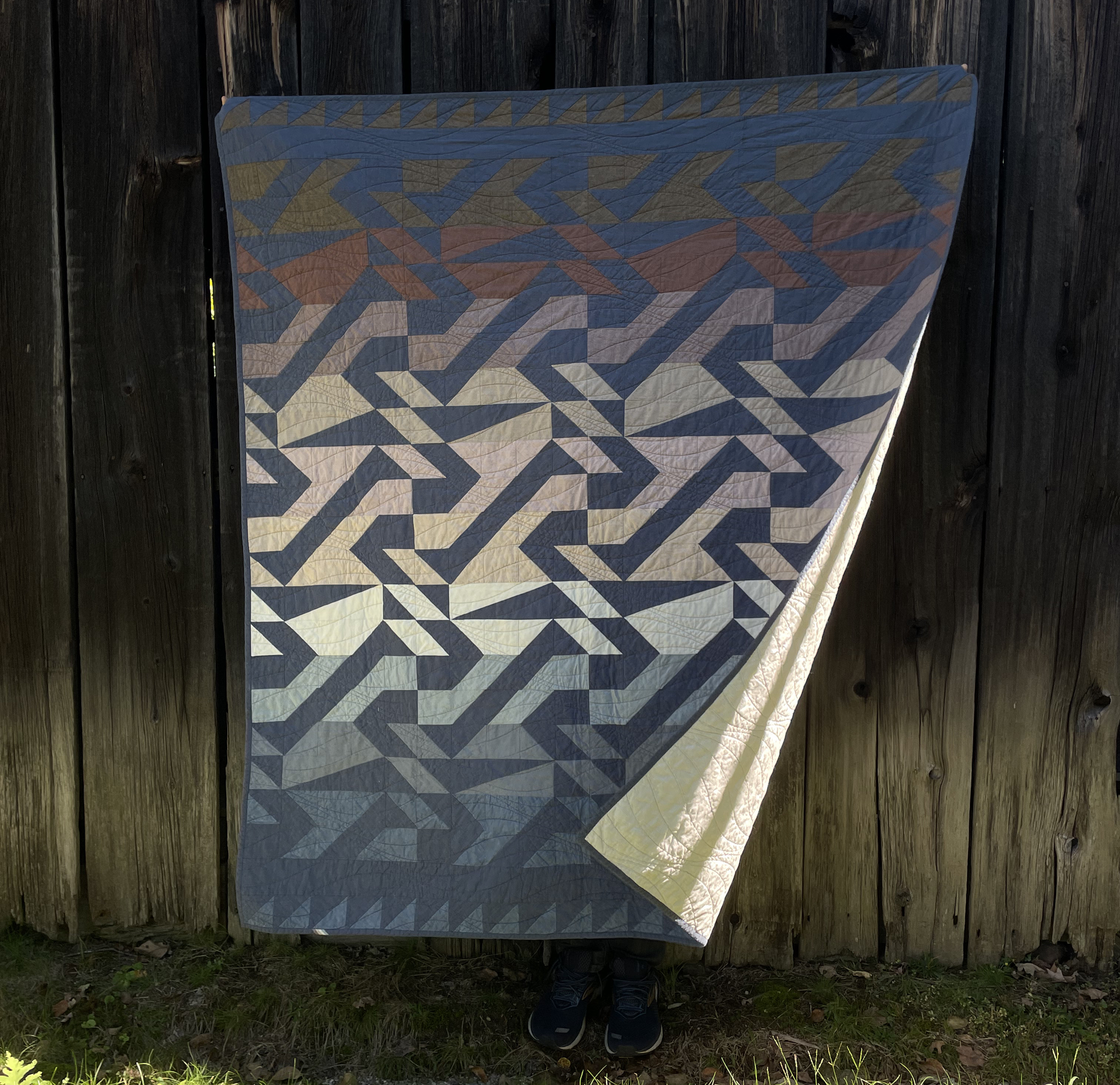 Quilt with a geometric pattern hanging on a wooden fence.