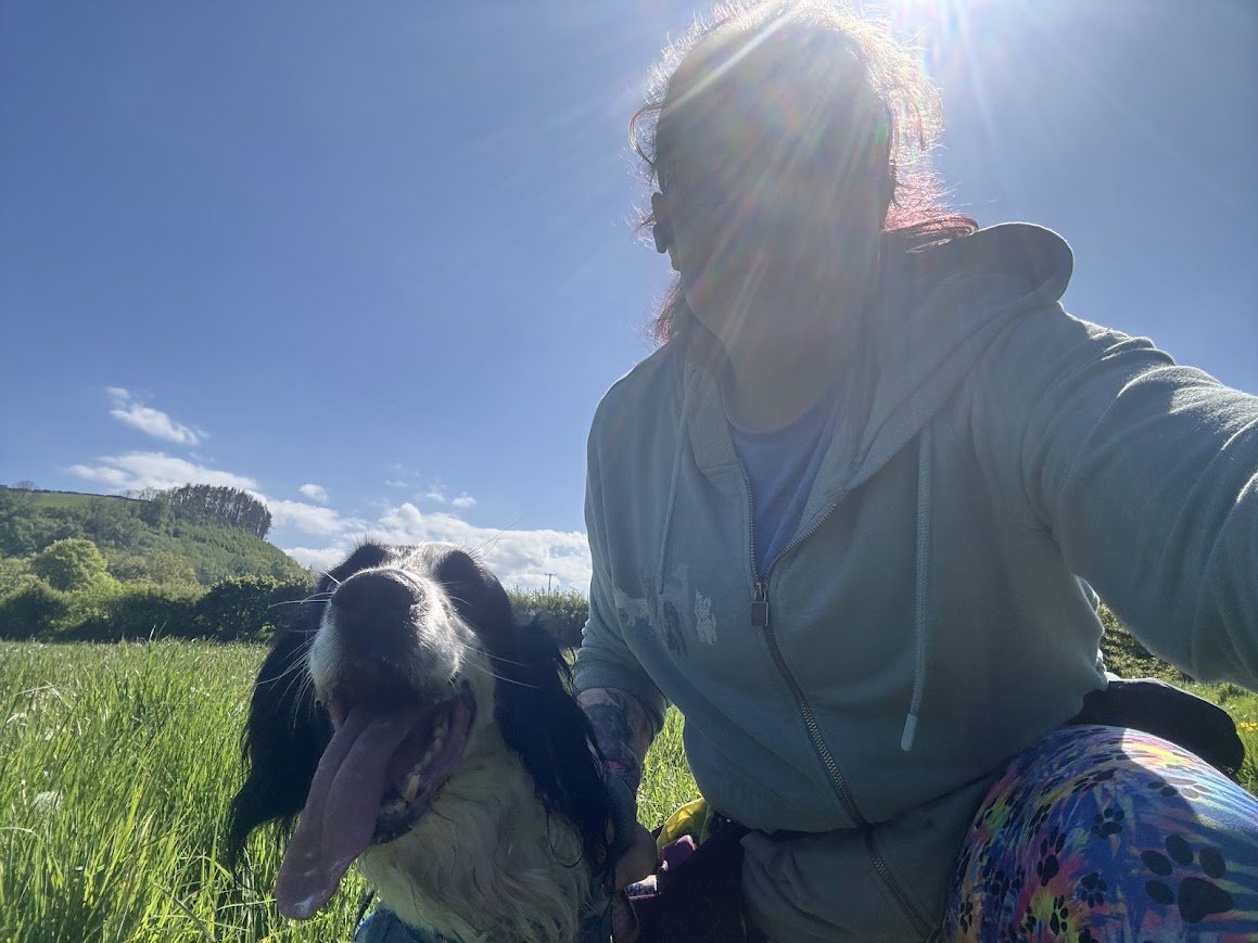 A person taking a selfie with a happy dog in a grassy field on a sunny day.