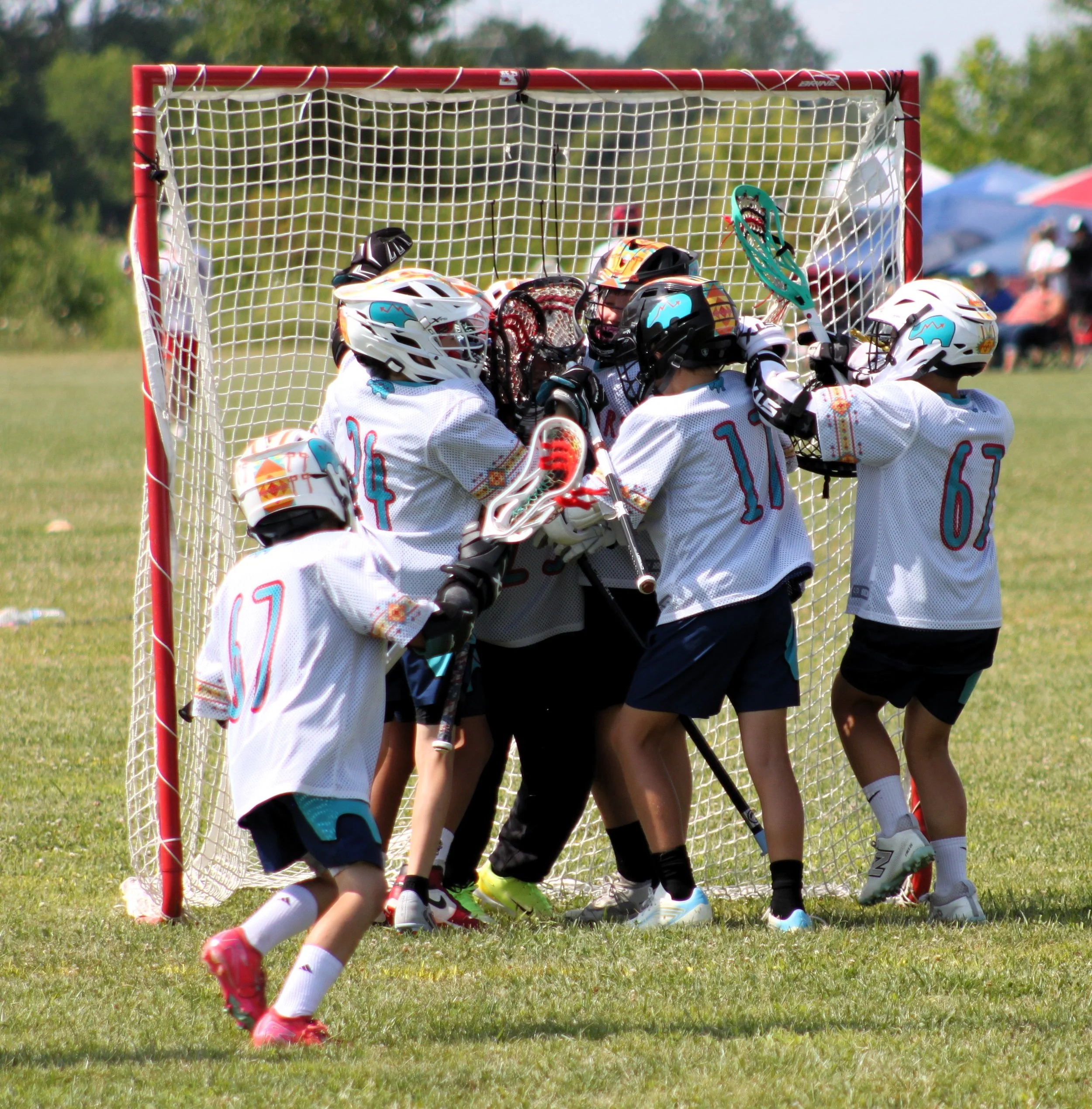 Children playing lacrosse near a goal on a grassy field during daytime.