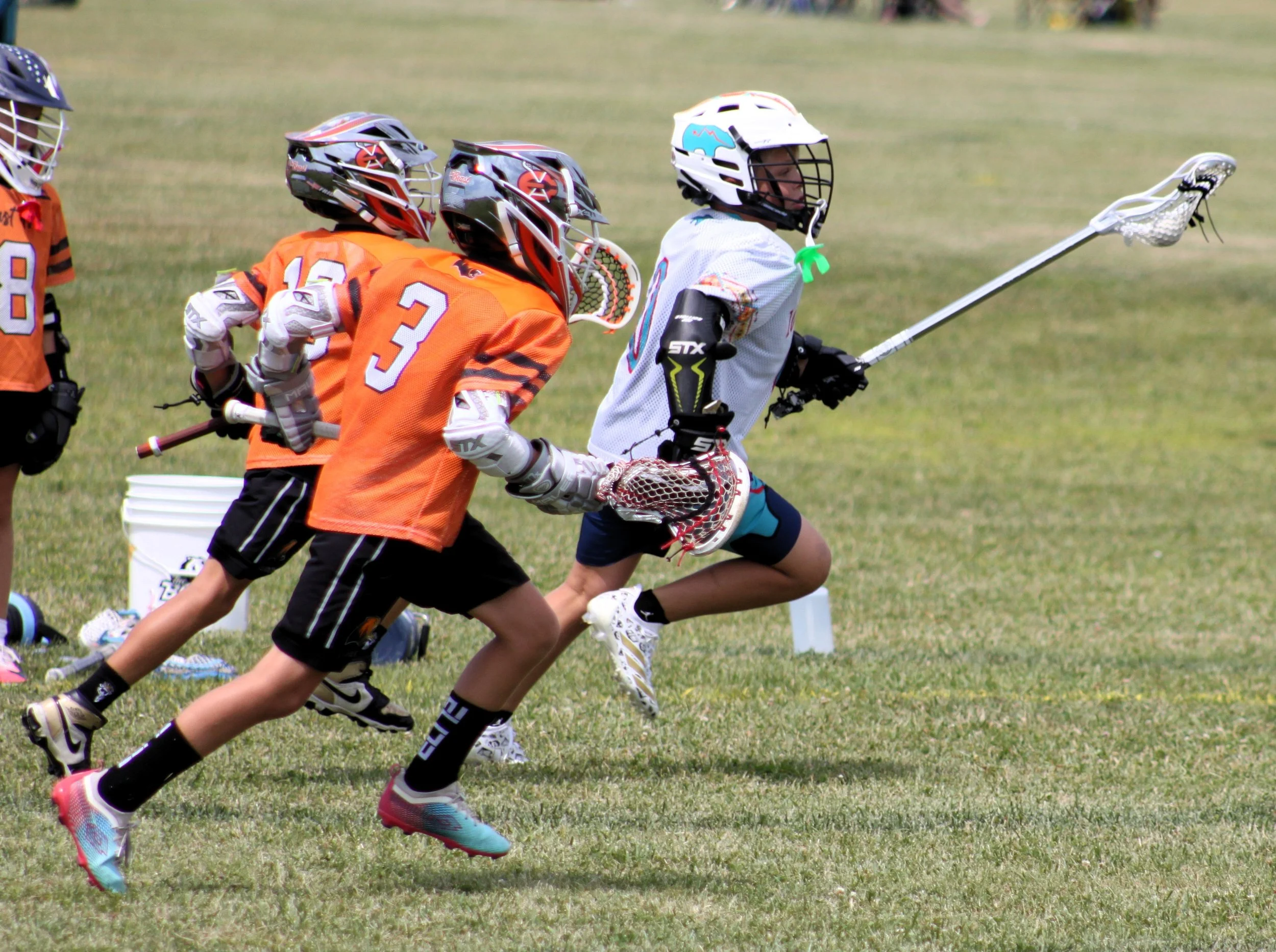 Lacrosse players in action on a grassy field, wearing helmets and sports gear, competing for the ball.
