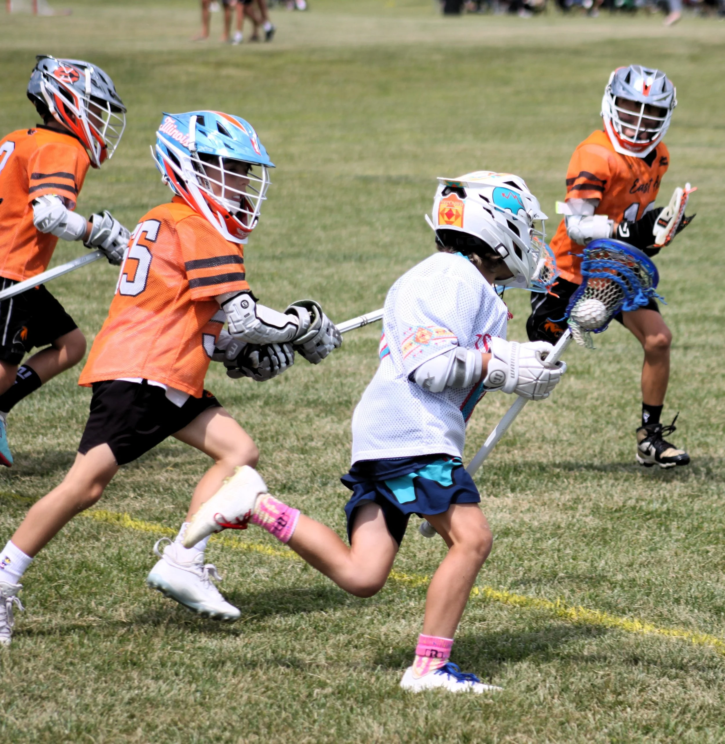 Children playing lacrosse on a grassy field, wearing helmets and sports uniforms.