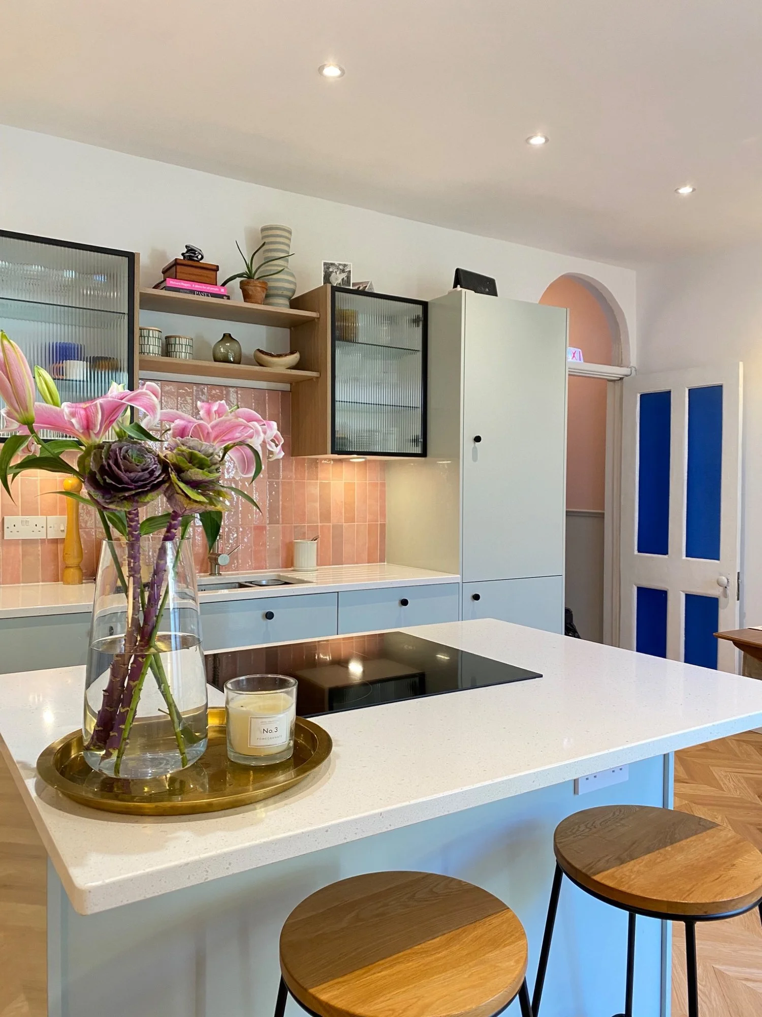 Kitchen at The Arch House in Easton, Bristol, with pale blue cabinets, a white island, pink tiles and a blue-panelled door.