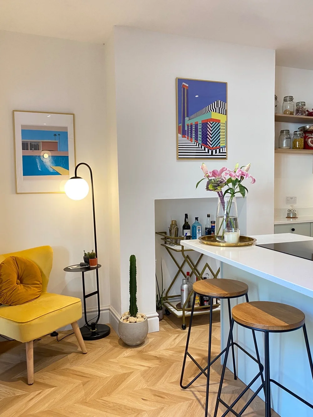 Kitchen and seating area at The Arch House in Easton, Bristol, with a white island, timber stools, framed artwork and a yellow armchair.